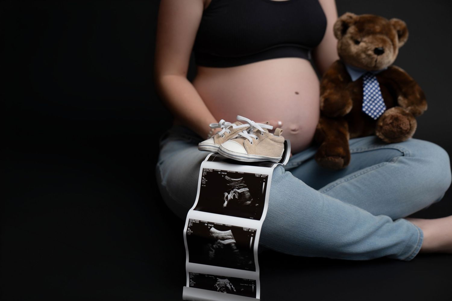 Maternity photo shoot with teddy bear props against dark background.