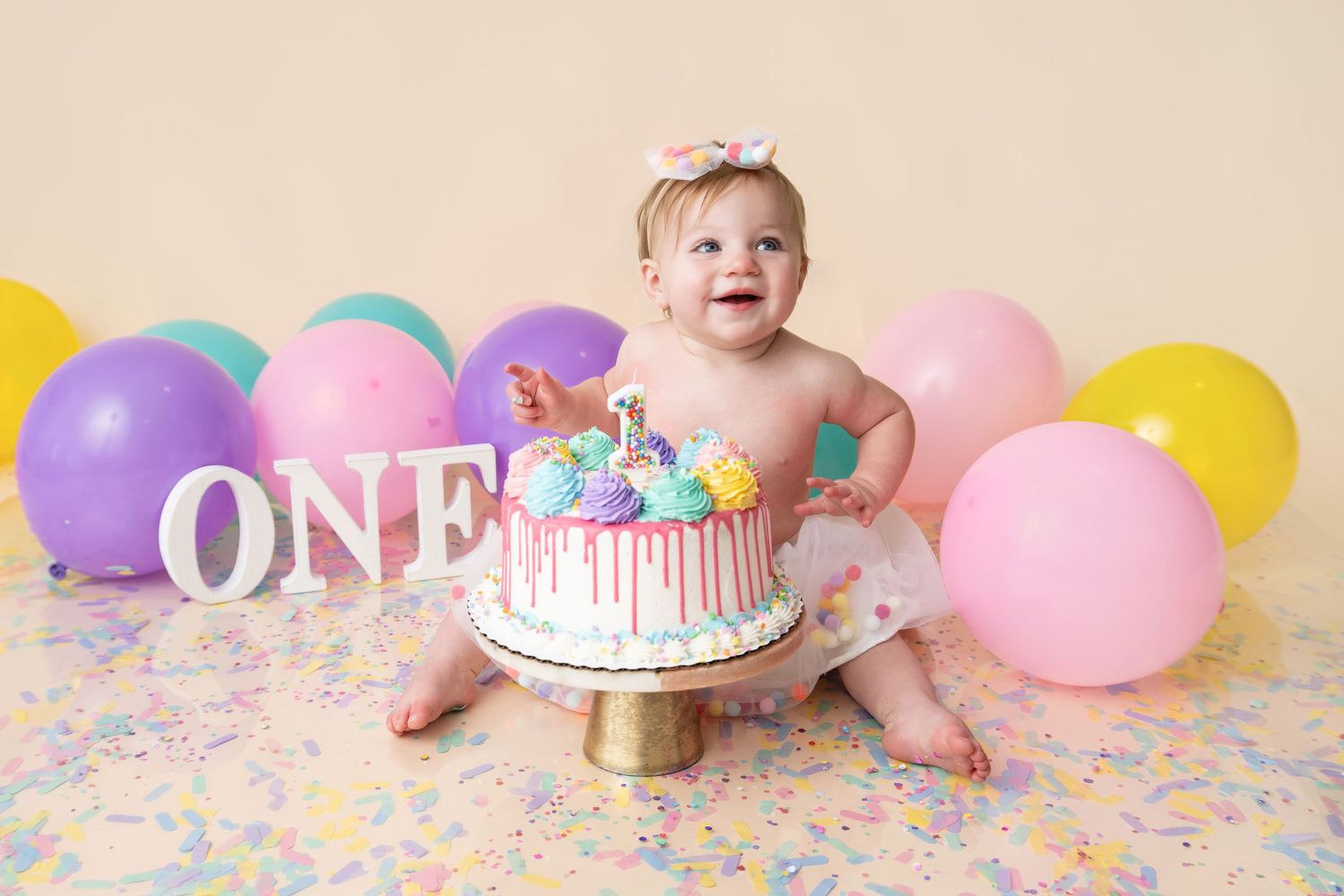 Baby girl smash cake first birthday photo with colorful balloons and ONE sign.