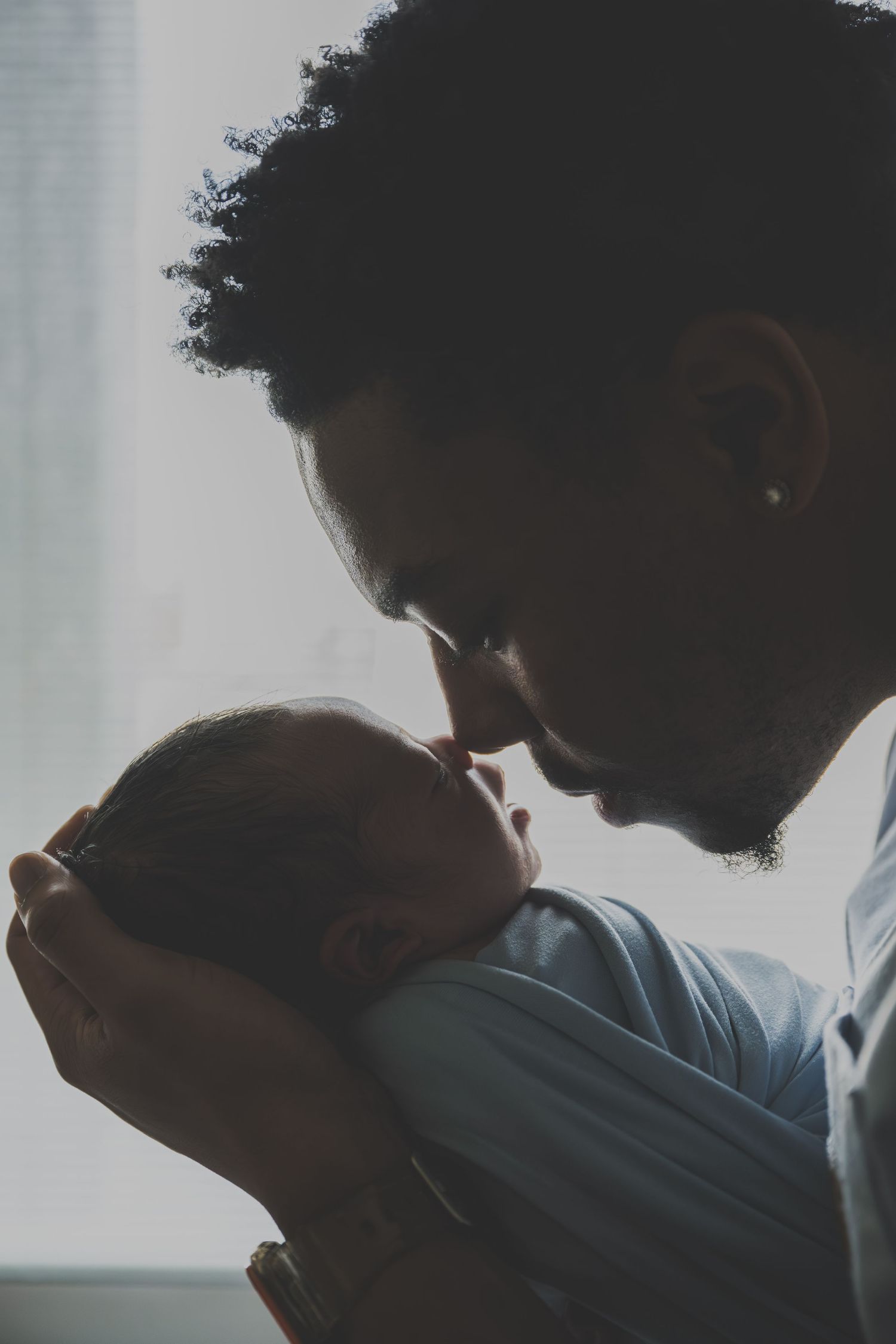 A father tenderly kisses his newborn baby's forehead in a softly lit room.