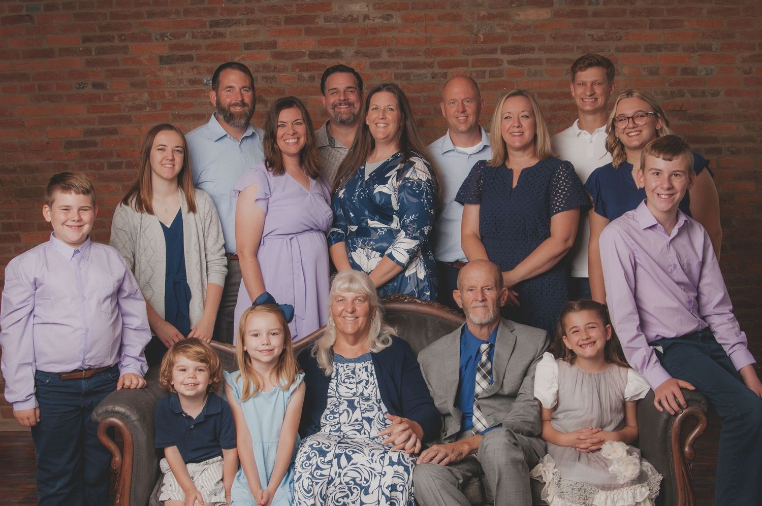 Large extended family poses together for portrait against rustic brick wall background.