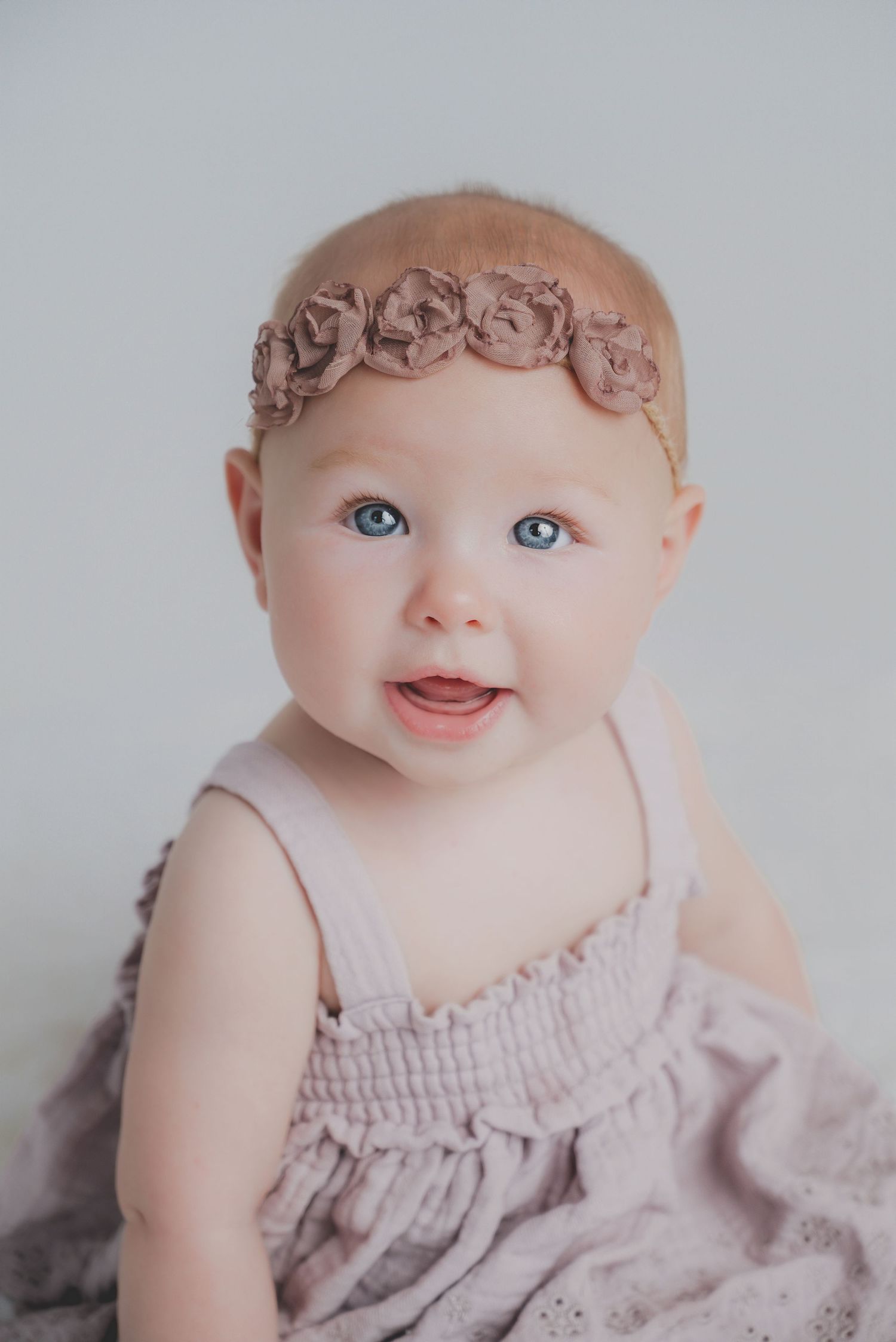 Baby wearing lace dress and headband smiles during portrait session.