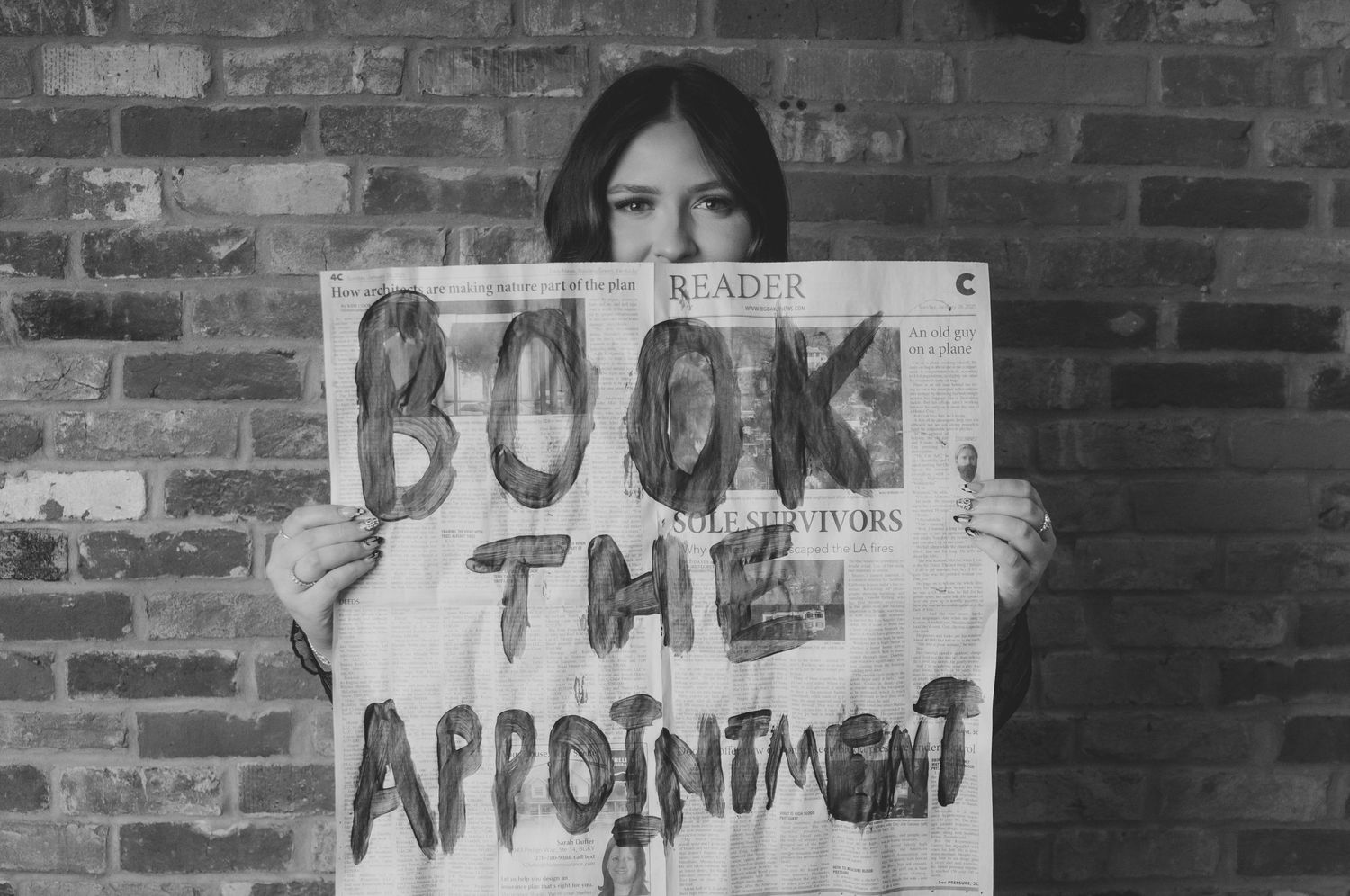 Person holding handwritten 'Book the Appointment' sign against brick wall. Studio photography franklin ky SOKY Branding Headshots