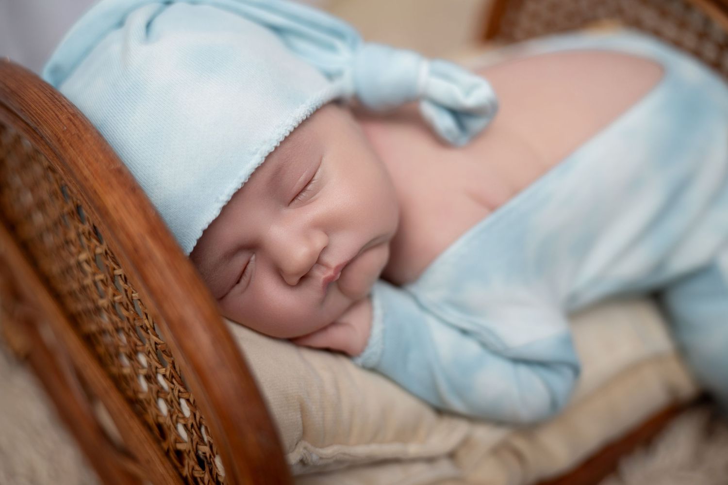 Sleeping baby wrapped in soft blue blanket resting in wooden rocking chair.