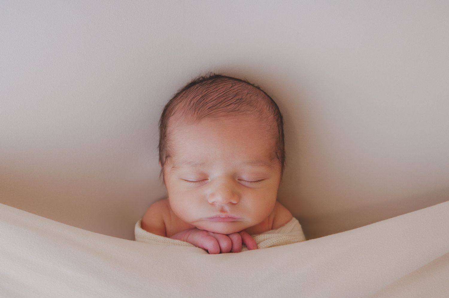Minimalist newborn portrait series featuring baby against light gray backdrop.