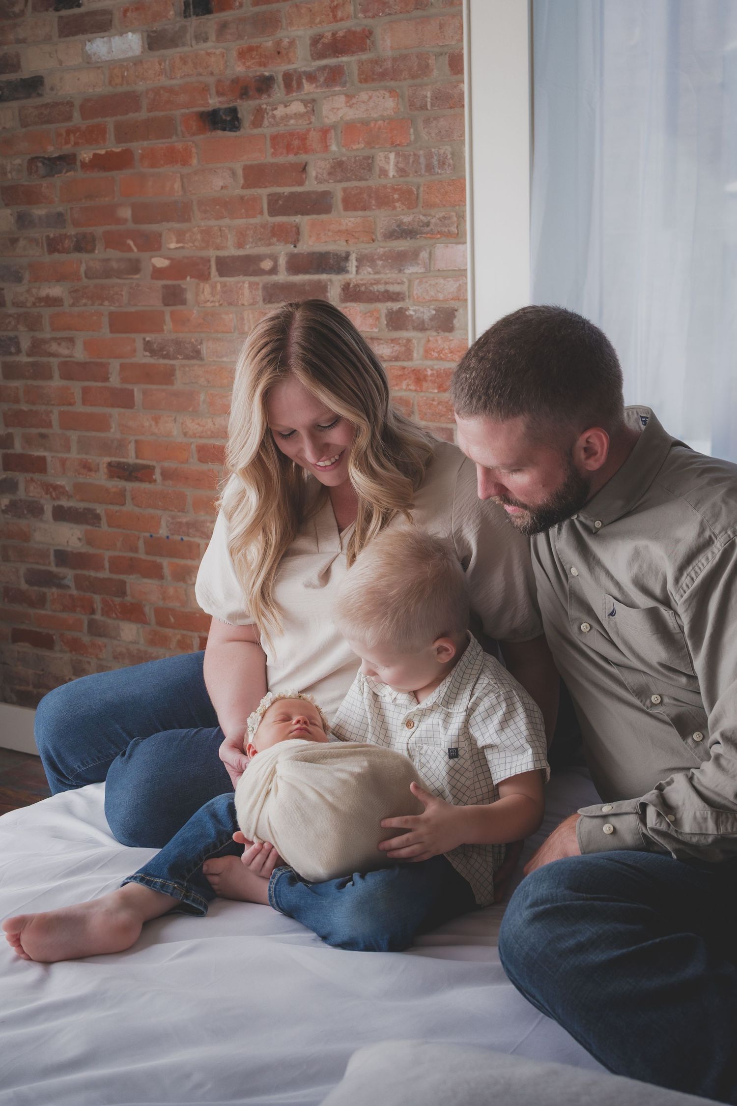 Family shares tender moment with baby on white bedding against brick wall. Studio photography franklin ky SOKY