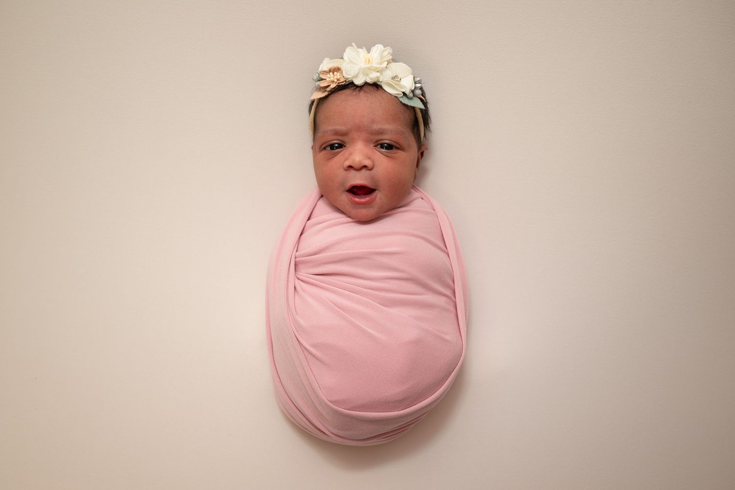 Newborn baby wrapped in soft pink swaddle against neutral beige background. in hospital newborn photography Bowling green ky glasgow ky