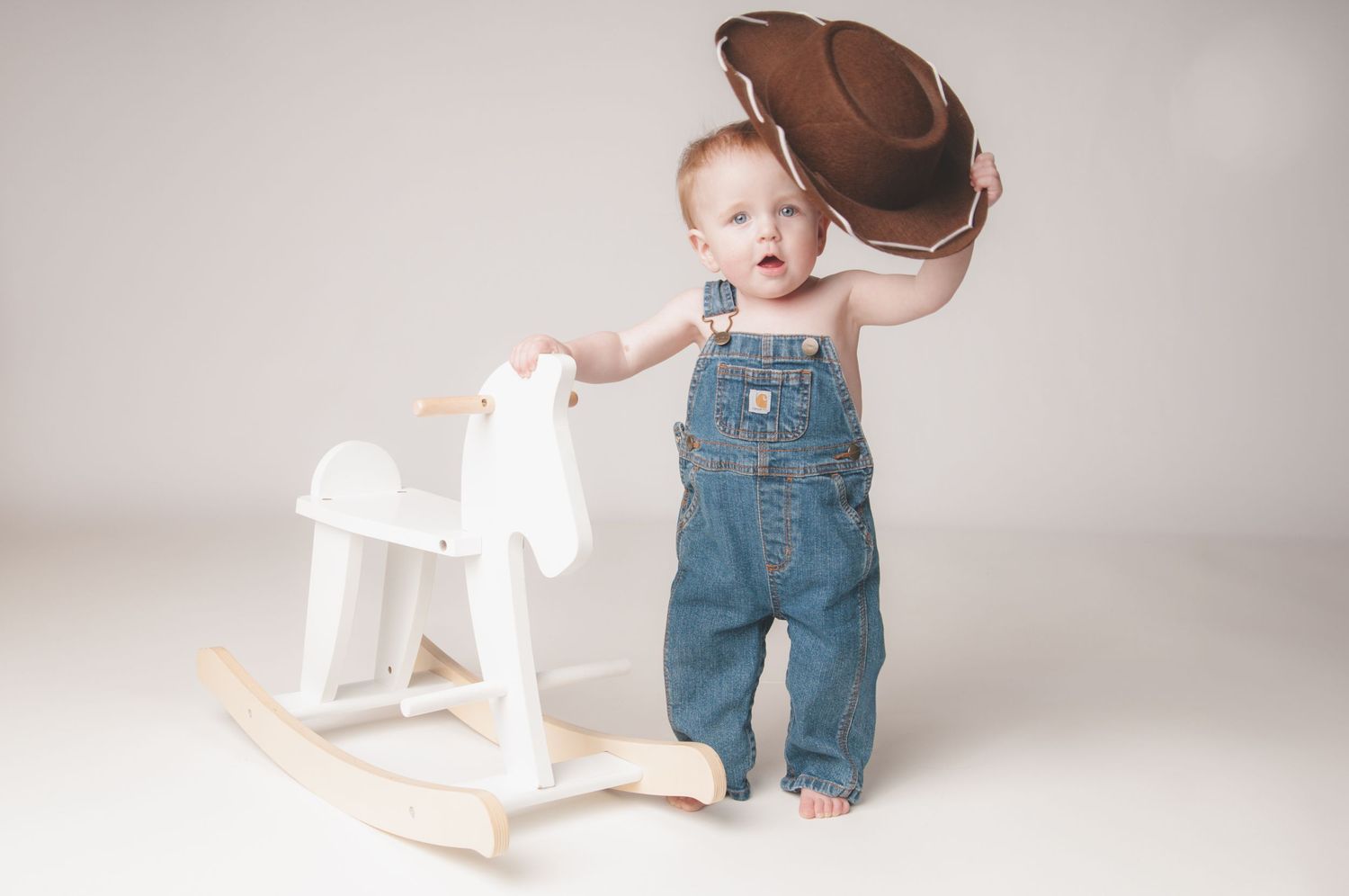 Baby milestone photos with white rocking horse prop in studio setting.