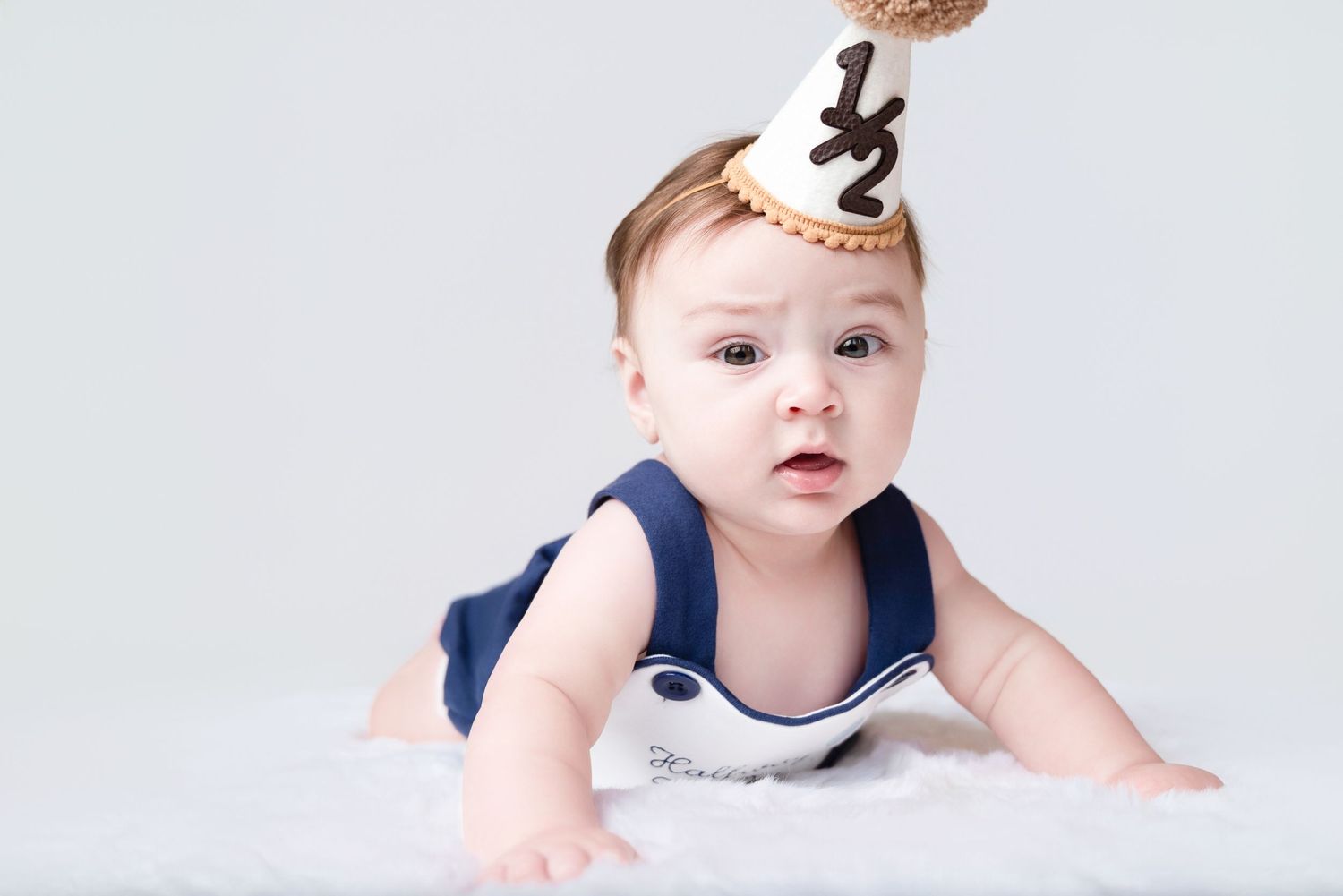 Baby milestone photo session with numbered props against white background.