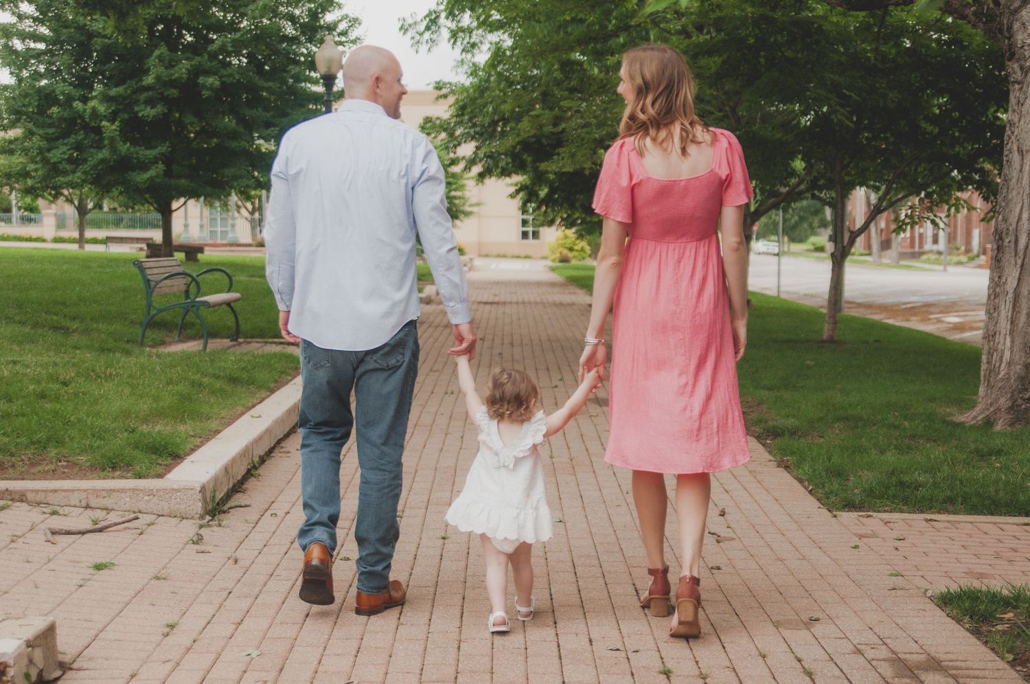 Family walking together on brick pathway through park on sunny day.