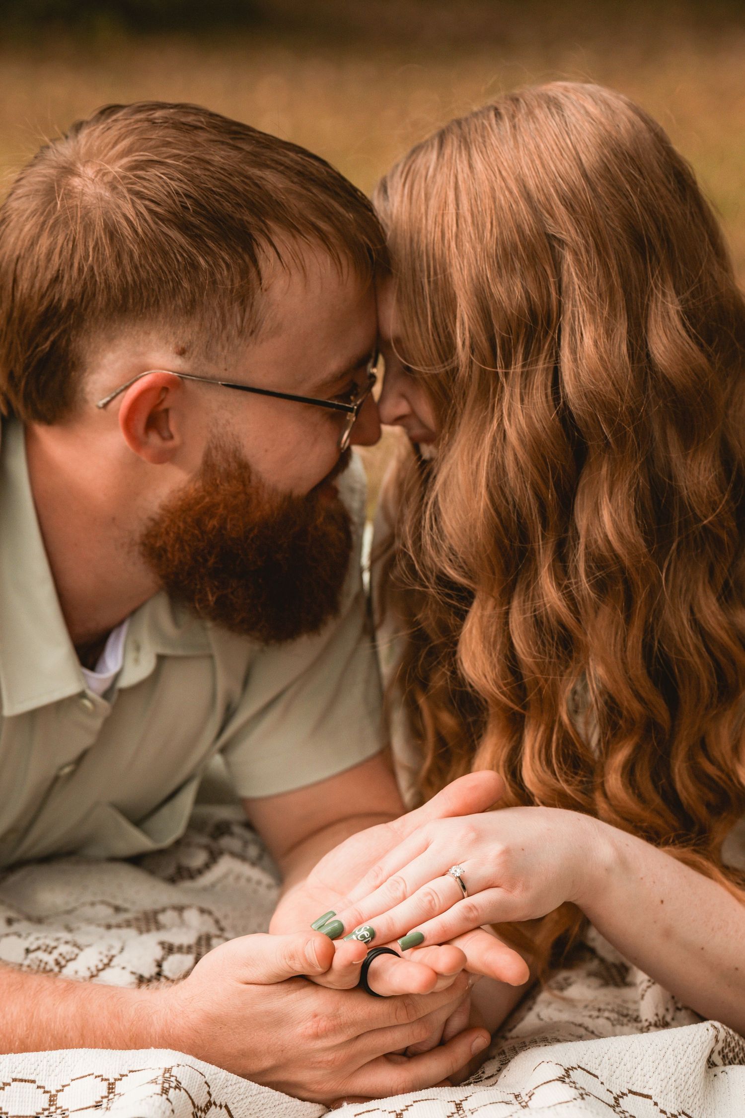 Close-up of couple holding hands with engagement ring in warm lighting.