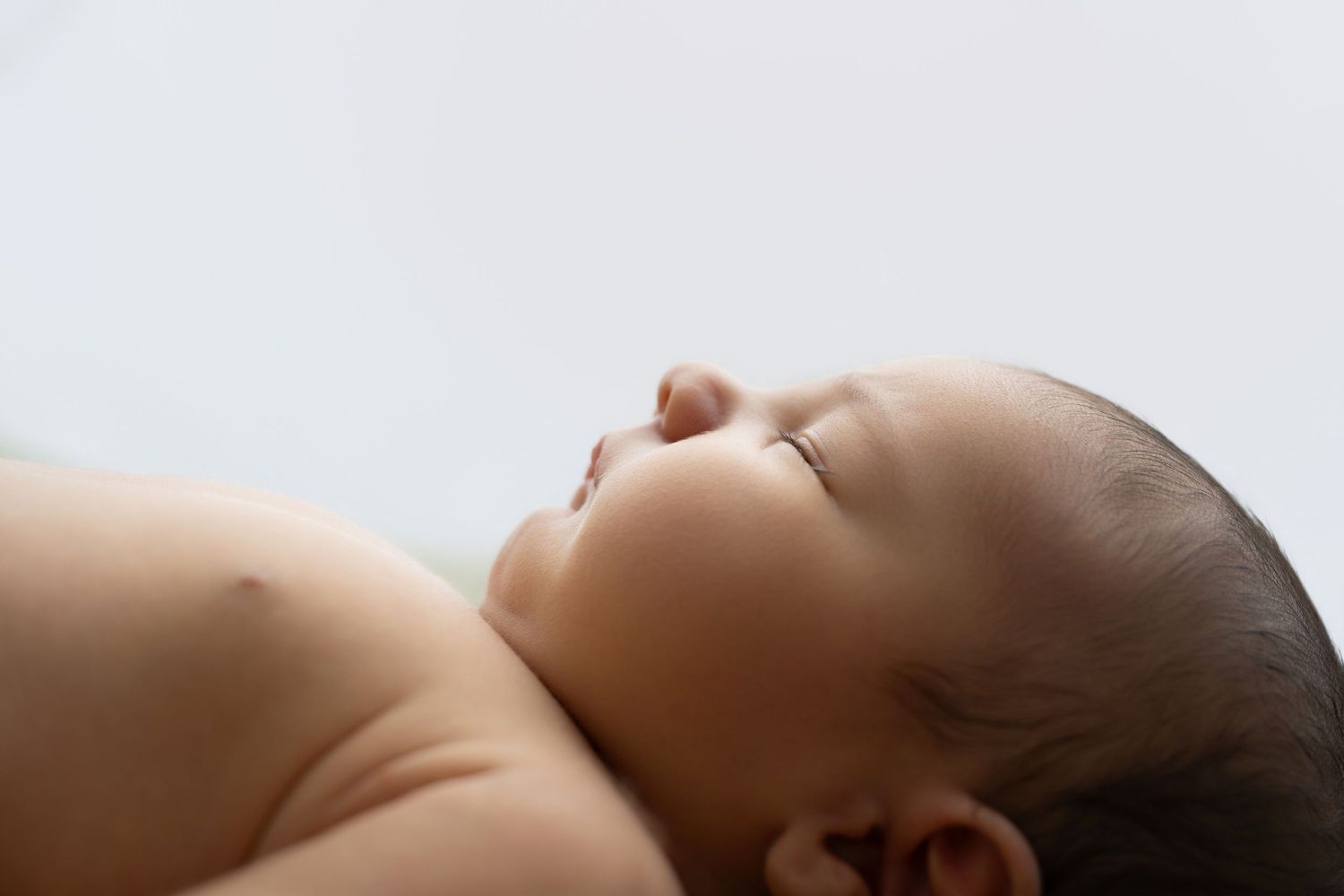 Peaceful newborn baby sleeping on its side with eyes closed, soft white background, close-up portrait photo.