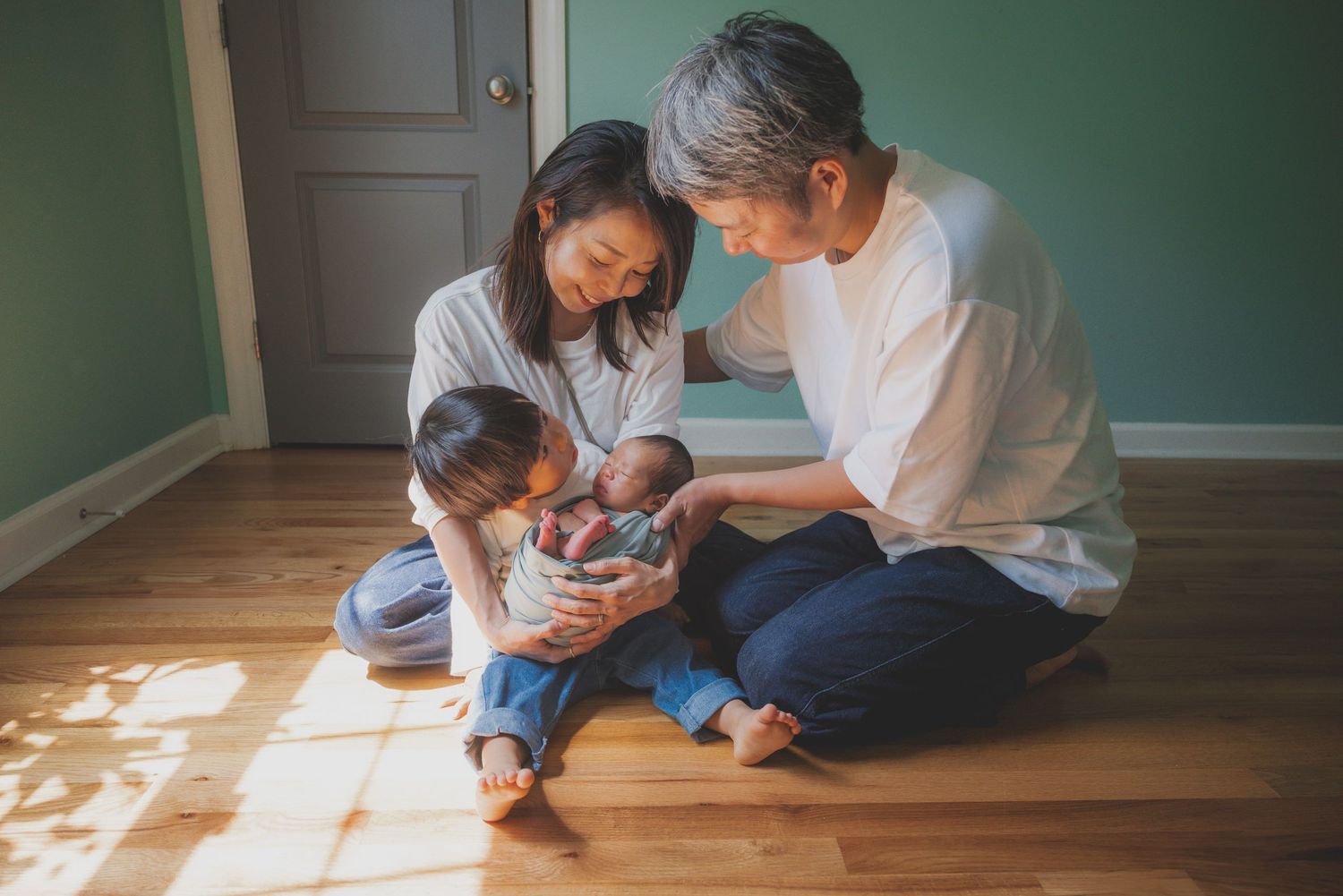 Family sitting together on hardwood floor in sunlit room.