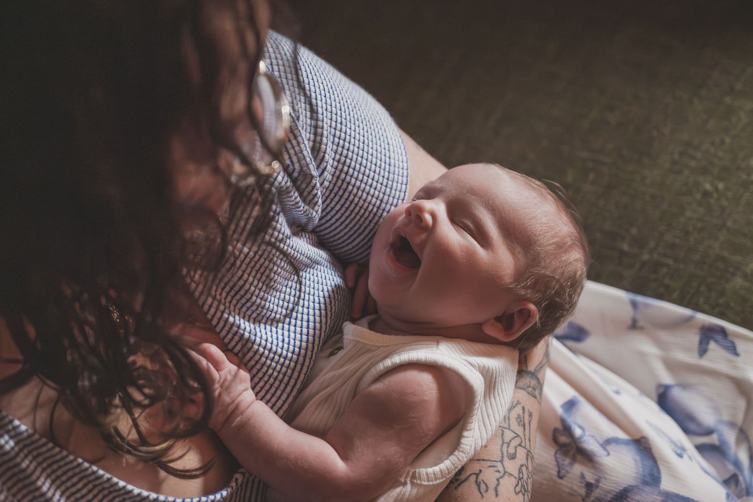 Newborn baby wearing white sleeps peacefully on textured fabric.