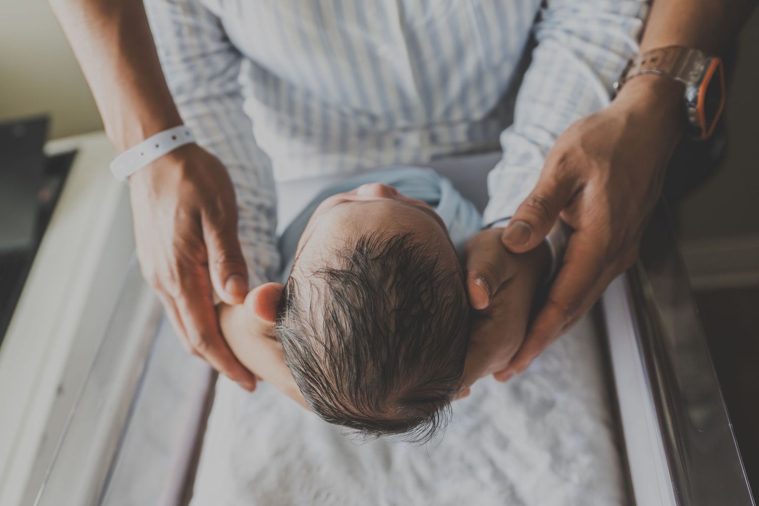 Adult hands gently cradling a newborn baby's head, captured from above in soft natural light.