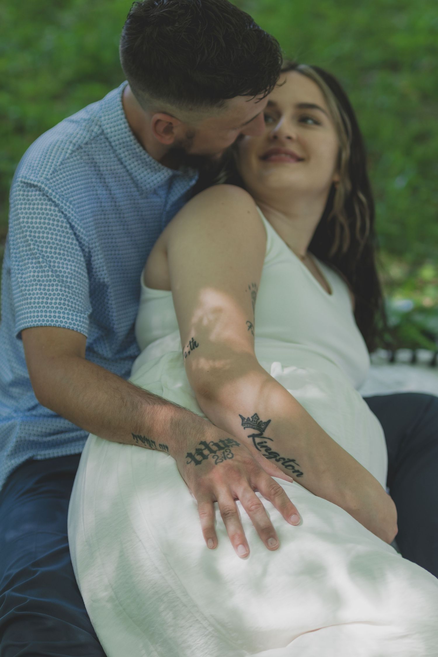 Romantic outdoor maternity photo session in white dress among greenery.