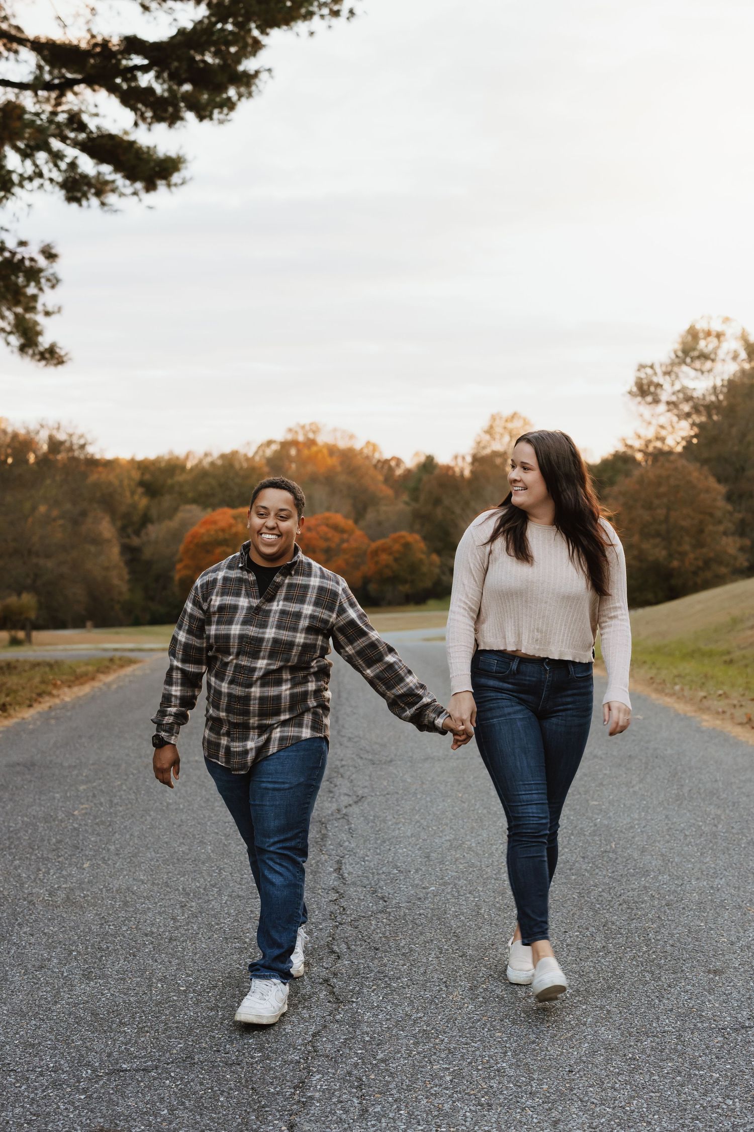 Two people walking together on a gravel path during autumn sunset wearing plaid shirts and jeans.