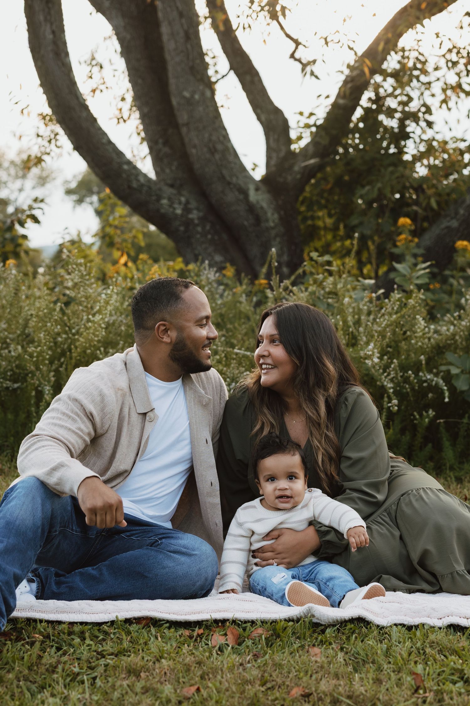 Happy family enjoying a picnic together on a blanket outdoors near a large tree on an autumn day.