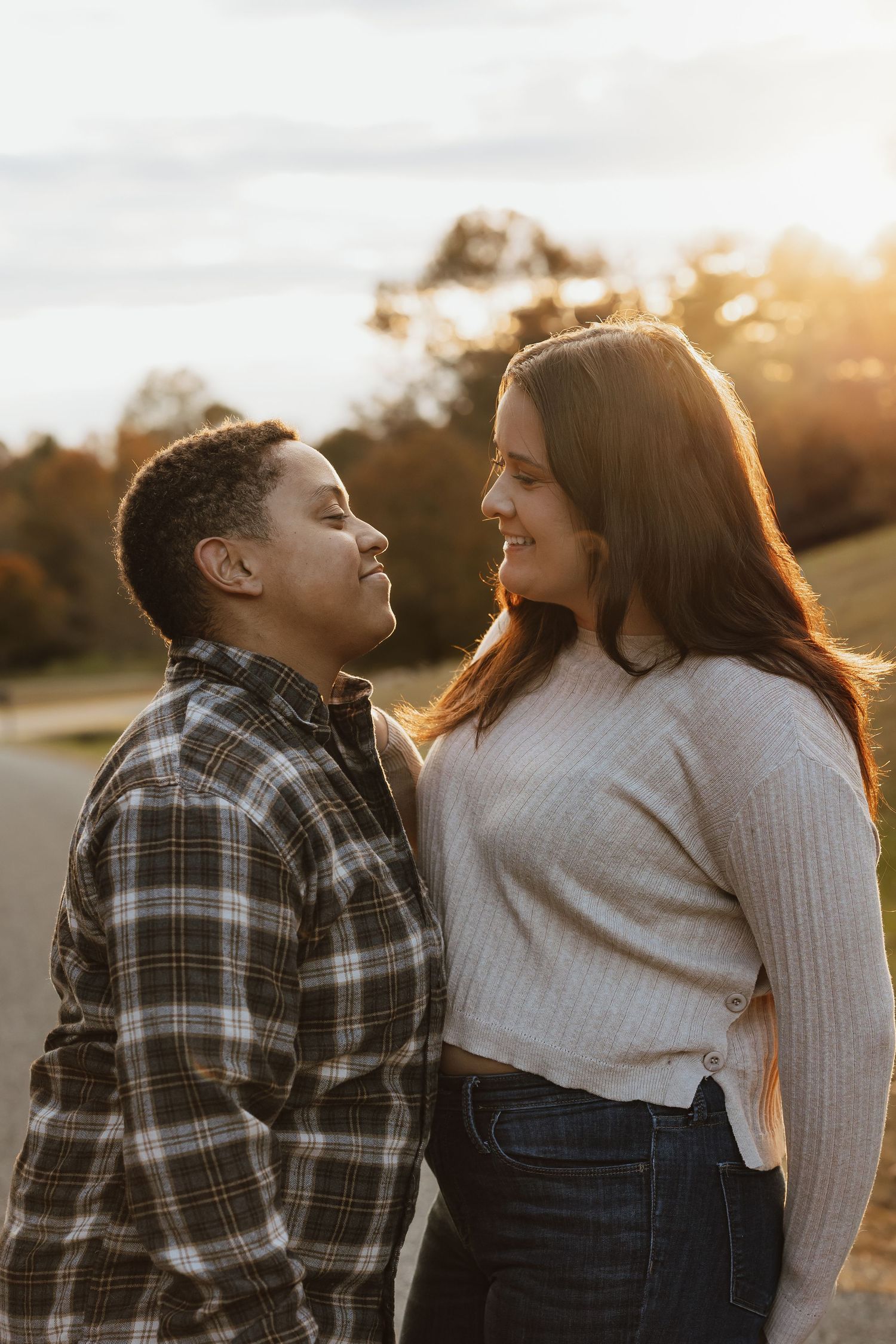 A romantic couple shares a tender moment at sunset, with golden light illuminating their smiling faces as they gaze at each other.