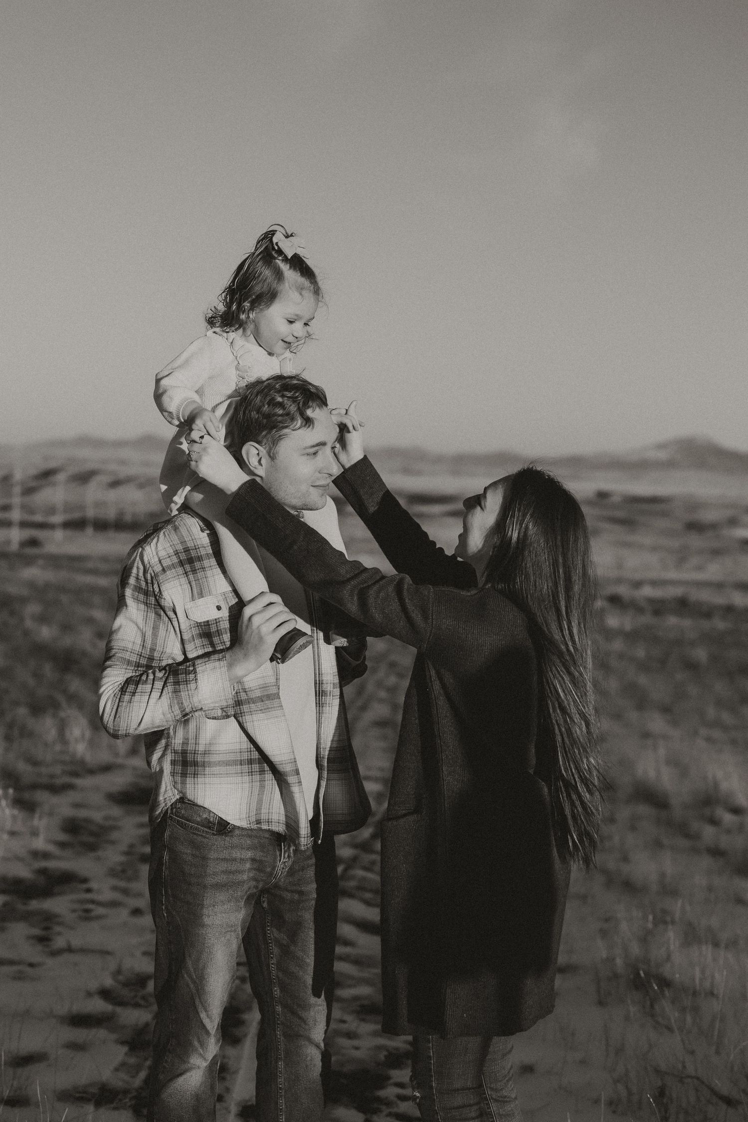 A couple shares tender moments in a series of black and white photos taken outdoors in a rural landscape.