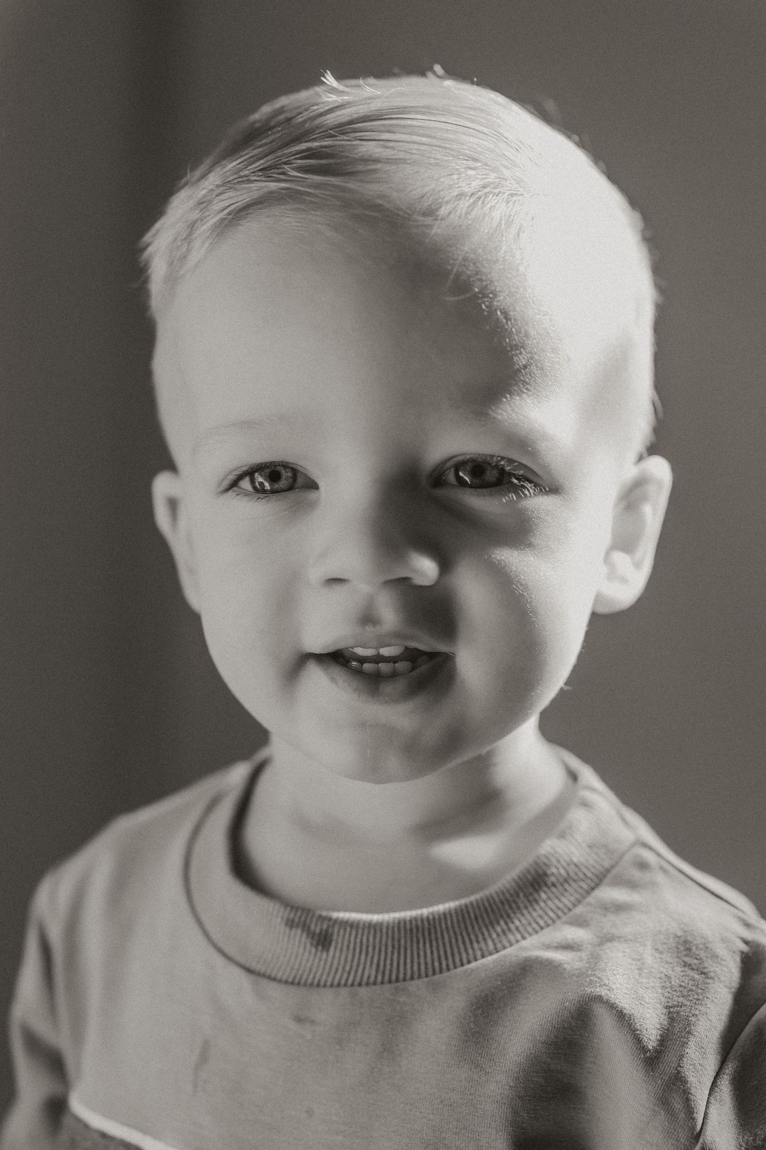 Black and white portrait series showing a baby's expressions ranging from serious to joyful in a light sweater.