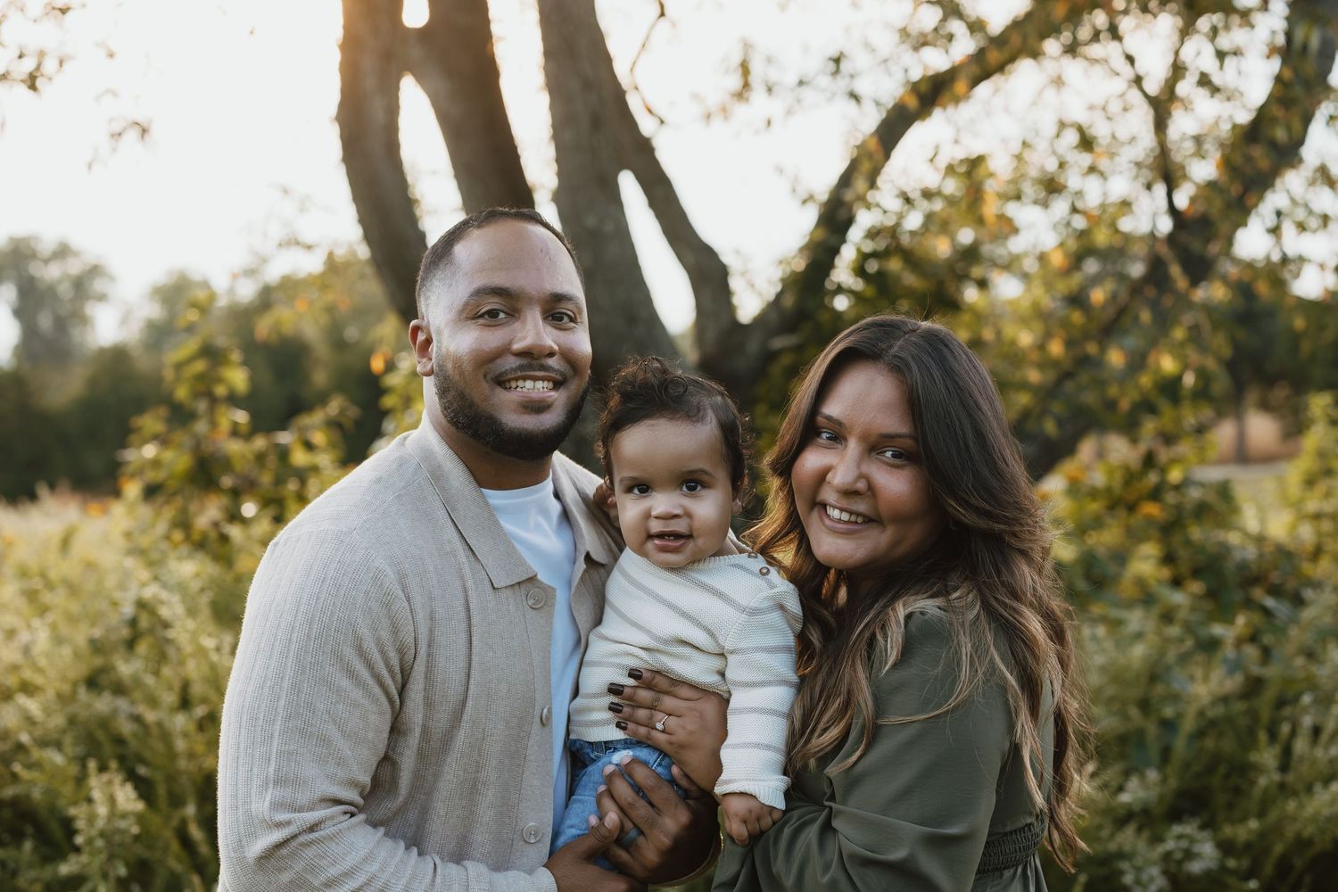 A family enjoying a warm autumn day outdoors together, laughing and embracing in golden sunlight.
