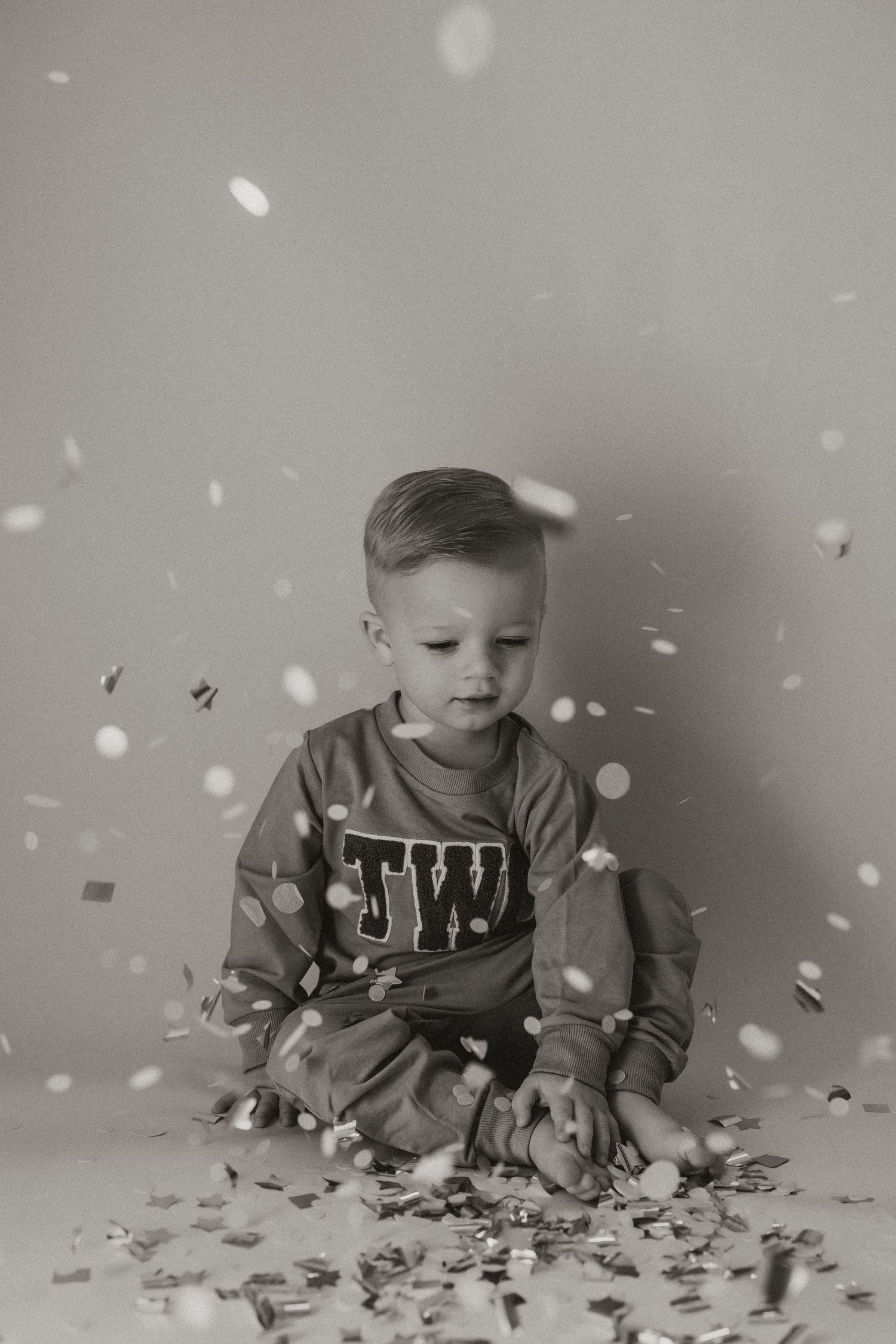 Black and white photo of a small child sitting on the floor while confetti falls around them.