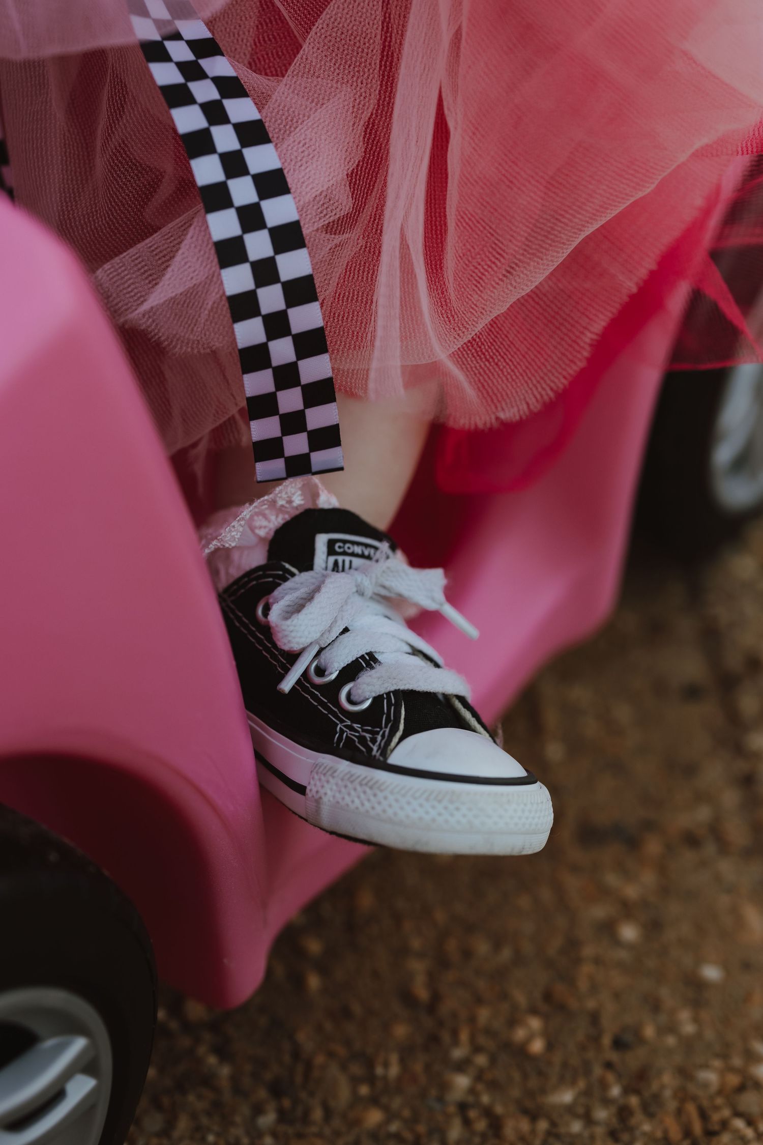 Black and white checkered sneakers peek out from under a flowing pink tulle skirt against a dark ground.