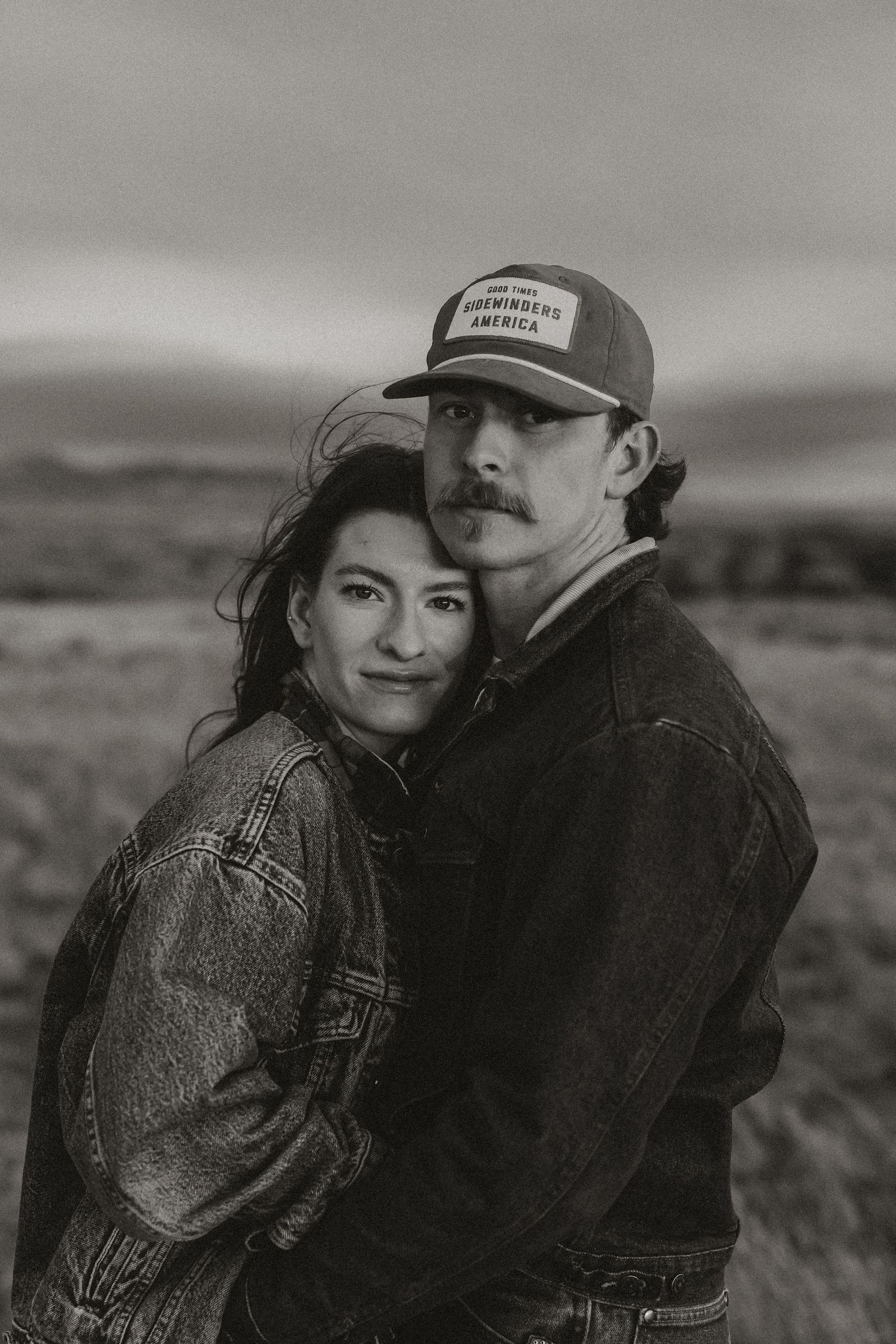 A romantic black and white photo series showing a couple embracing outdoors in a rural landscape.