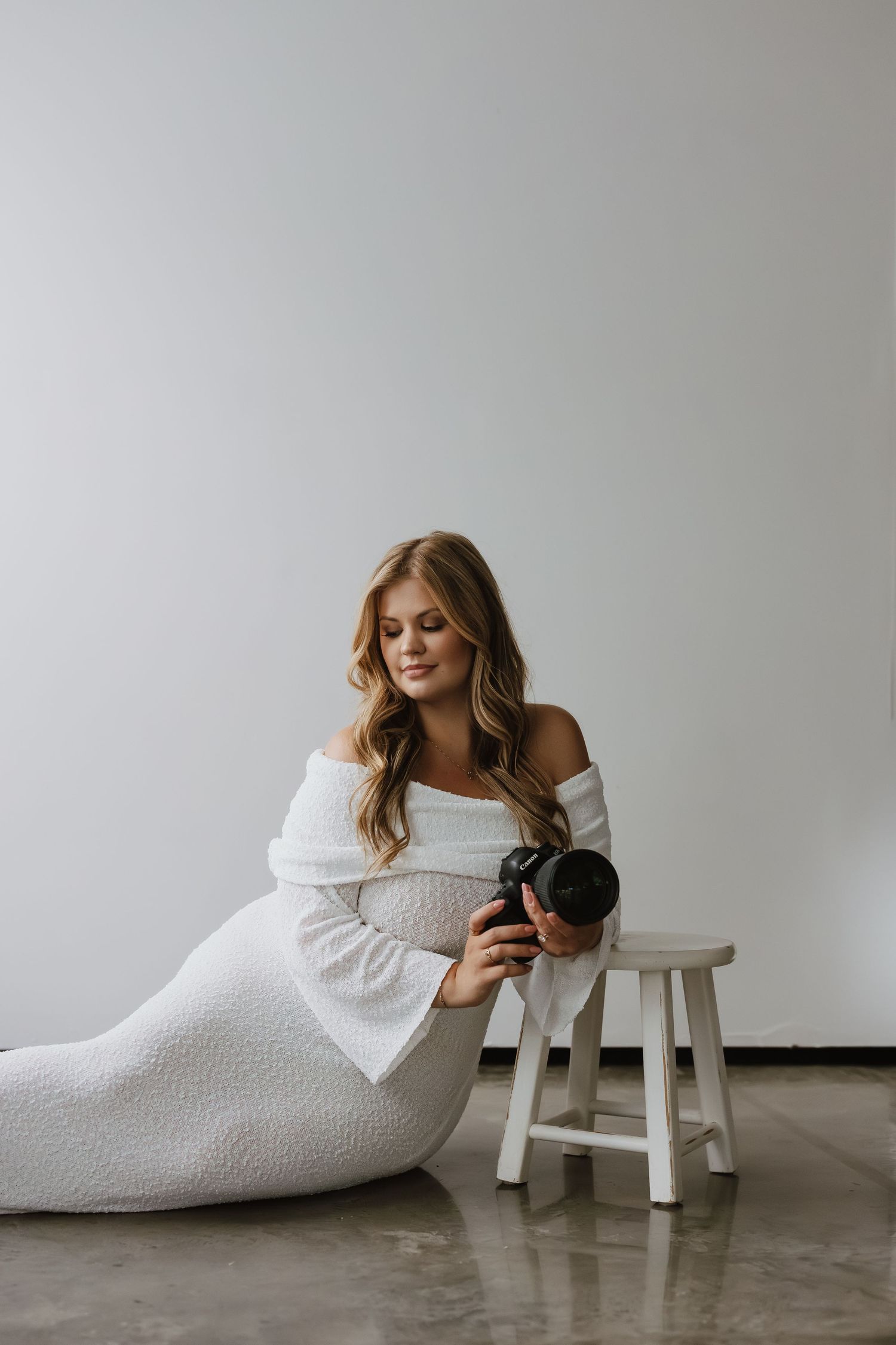 A series of minimalist portraits showing someone in a white dress lounging against a small wooden stool on a gray floor.