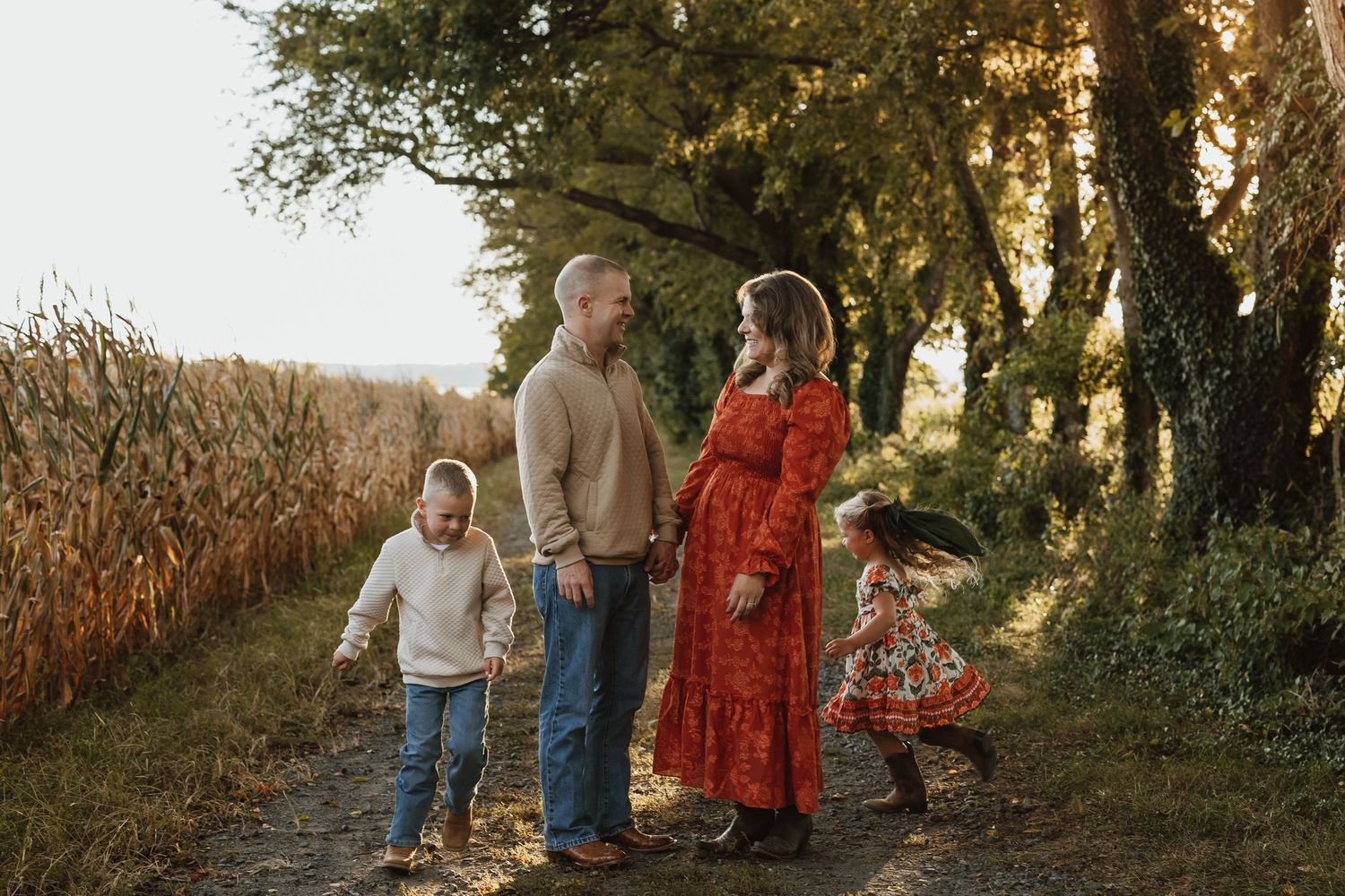 A family walks together during golden hour in a scenic outdoor setting with trees and cornfields in autumn.
