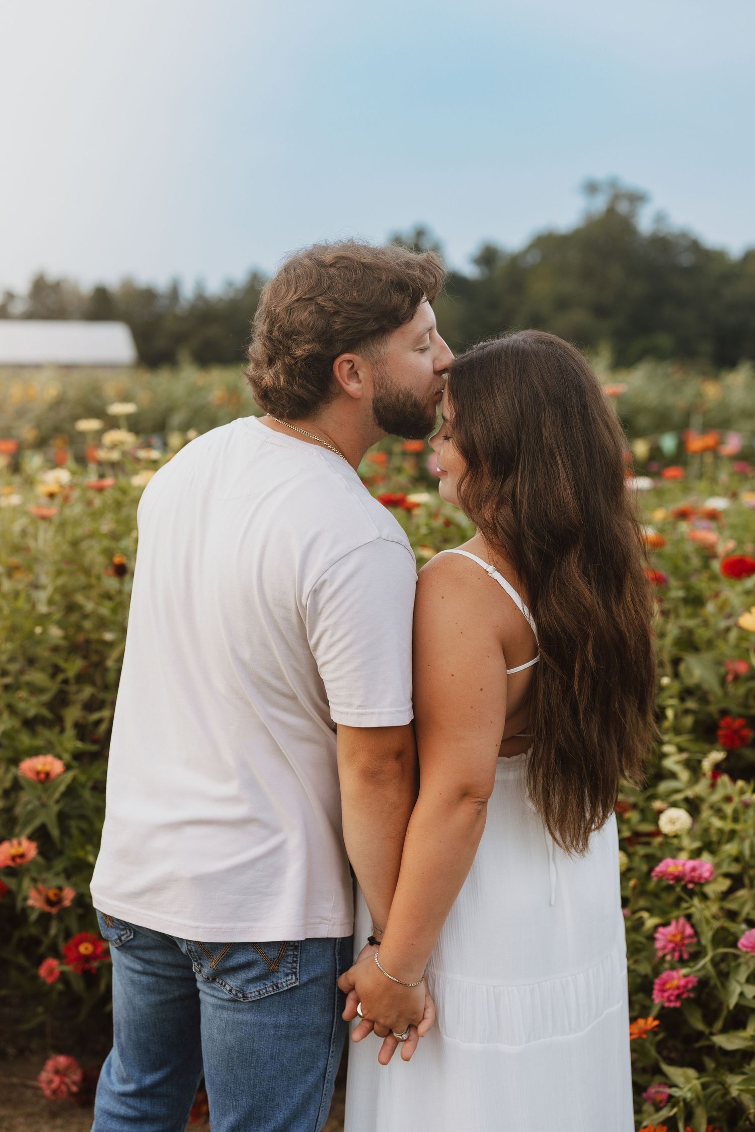 Couple embraces while standing in a colorful garden of blooming roses on a sunny summer afternoon.