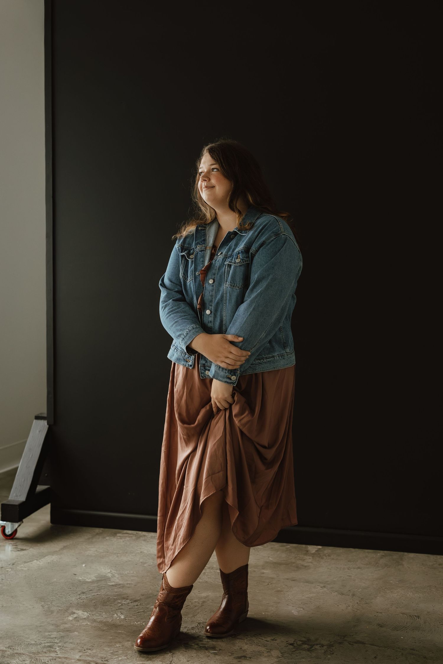 A series of moody portraits showing a person in a denim jacket and brown skirt sitting against a dark wall.