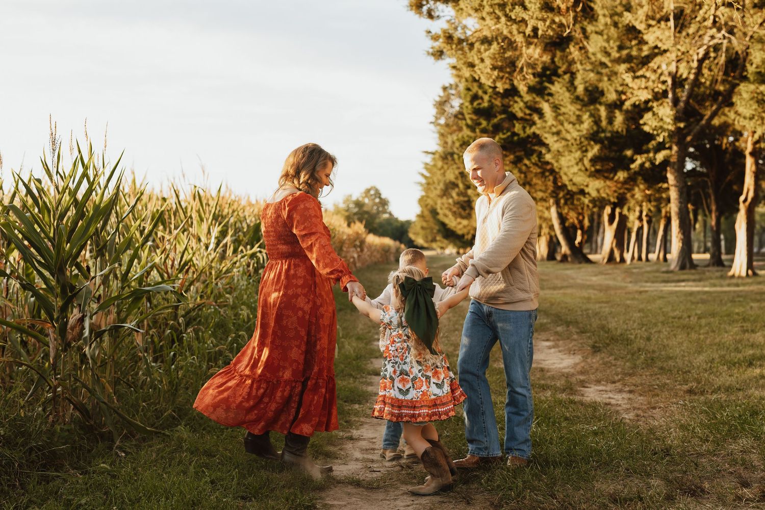 A family enjoying a sunset photoshoot in a golden field with tall grass and trees in the background.