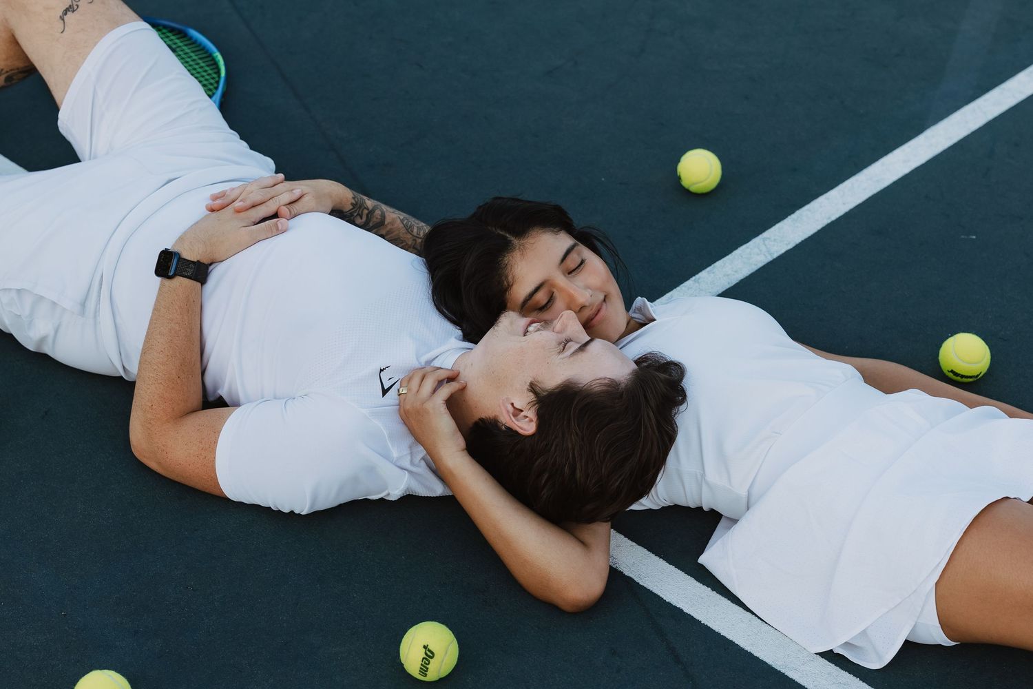 Tennis player lies on court surrounded by scattered tennis balls during a creative sports photoshoot.