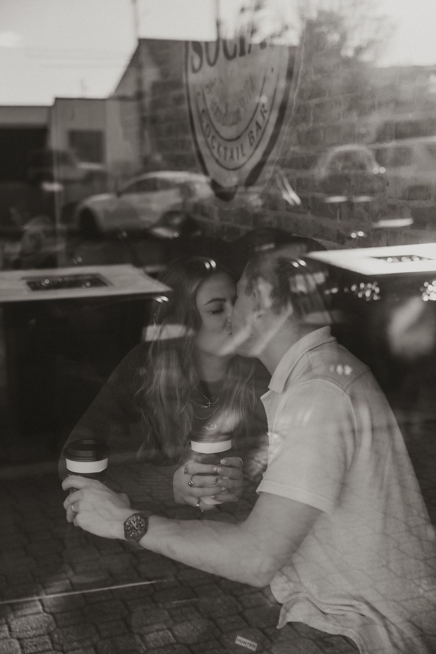 A black and white photo shows people through a reflective window at a coffee shop, creating a layered, artistic composition.