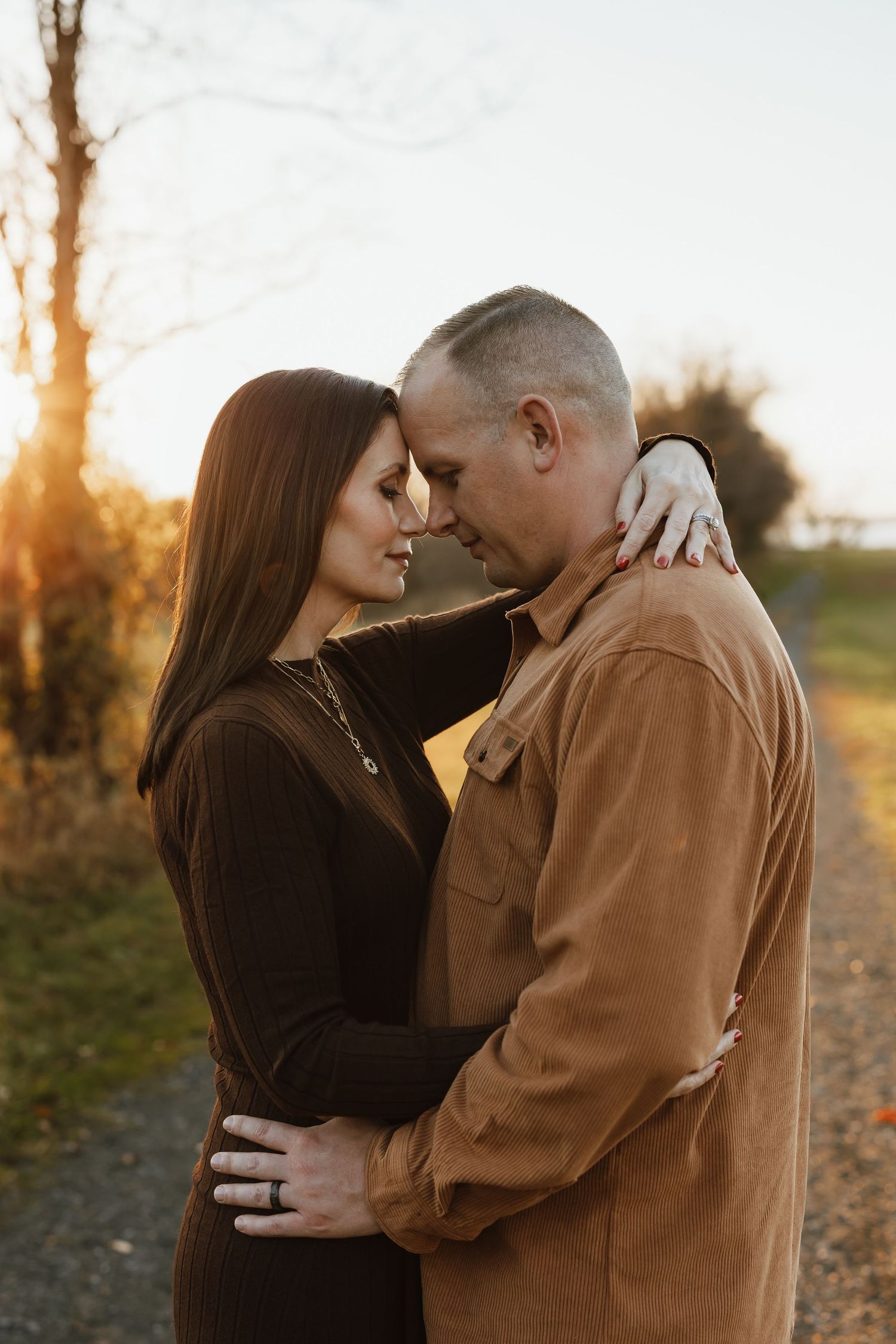 A romantic couple embraces in a tender moment at sunset with golden light filtering through trees in the background.