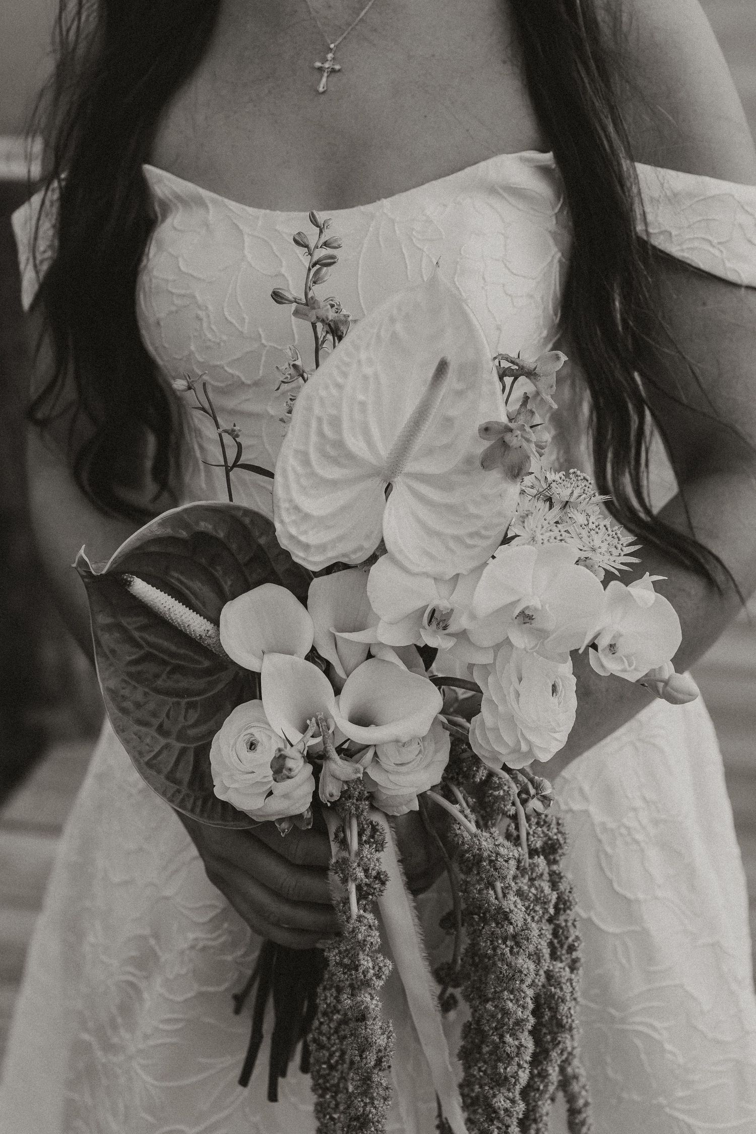 Black and white photo of a bride in a strapless lace gown holding a bouquet with anthuriums, orchids, and ranunculus.
