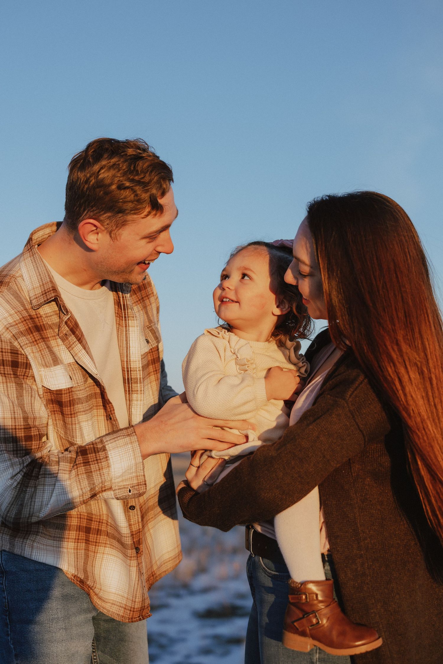 A family shares a joyful moment together outdoors during golden hour with a blue sky backdrop.