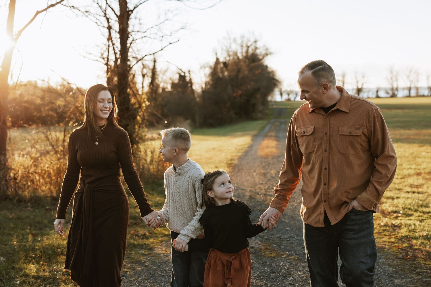 A family enjoys golden hour together in an autumn field wearing coordinating brown and neutral tones.