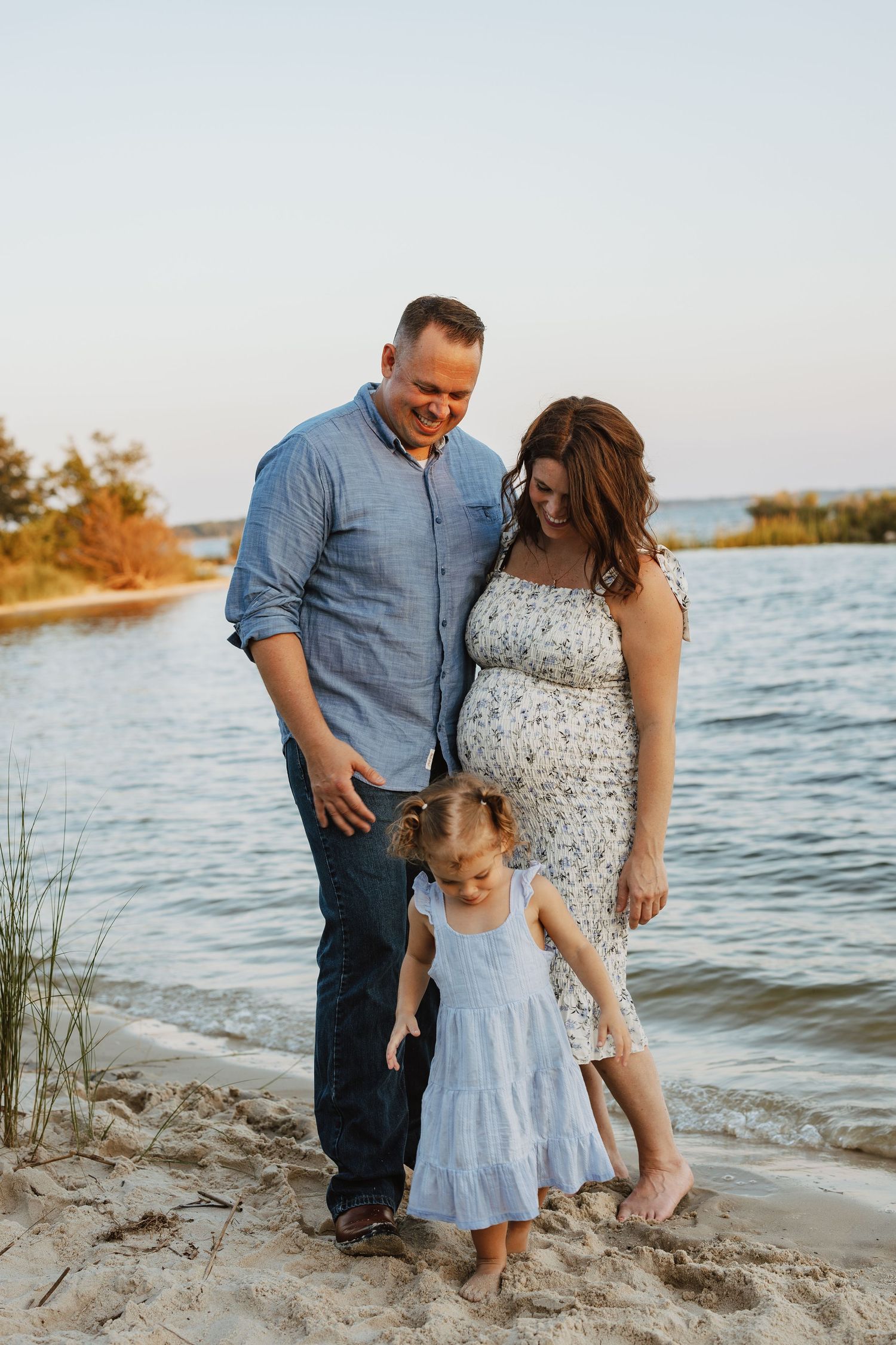 A family shares tender moments together while walking along a sandy beach at sunset near the water's edge.