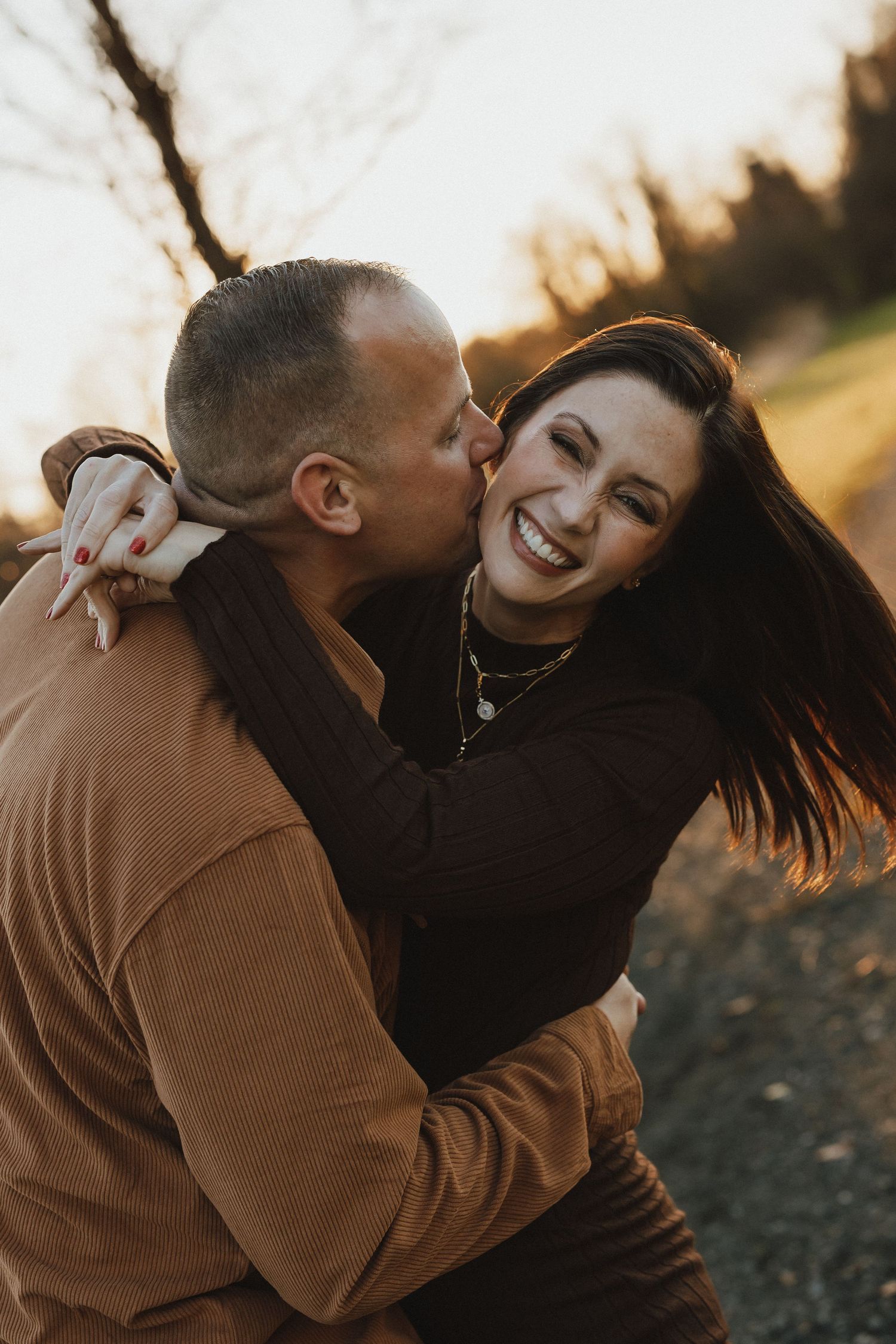 A couple embraces and laughs together during a golden hour photoshoot outdoors.