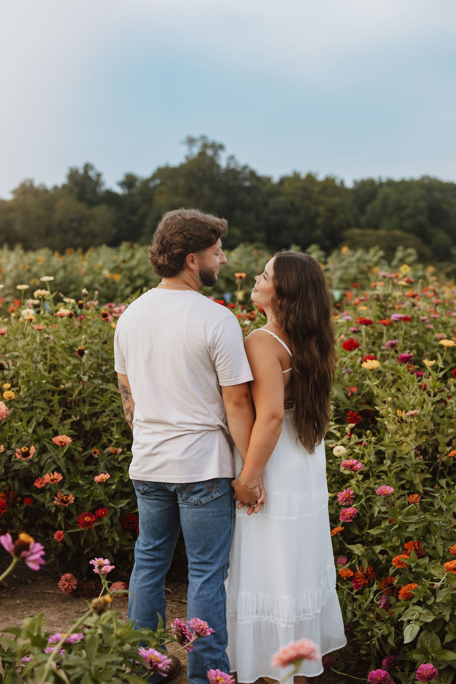A couple embraces while standing in a vibrant flower field filled with colorful blooms on a sunny afternoon.
