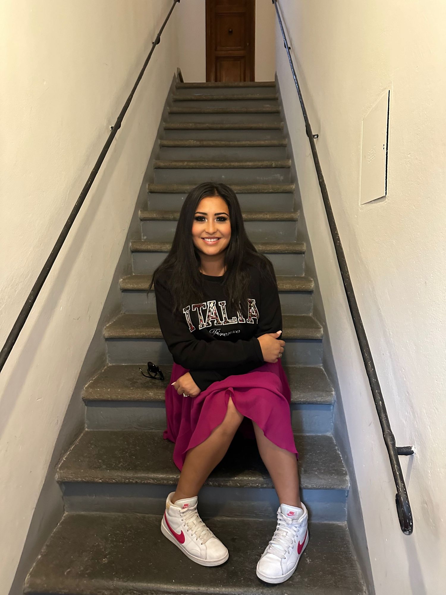 Person sitting on grey concrete stairs wearing casual clothing and white sneakers.