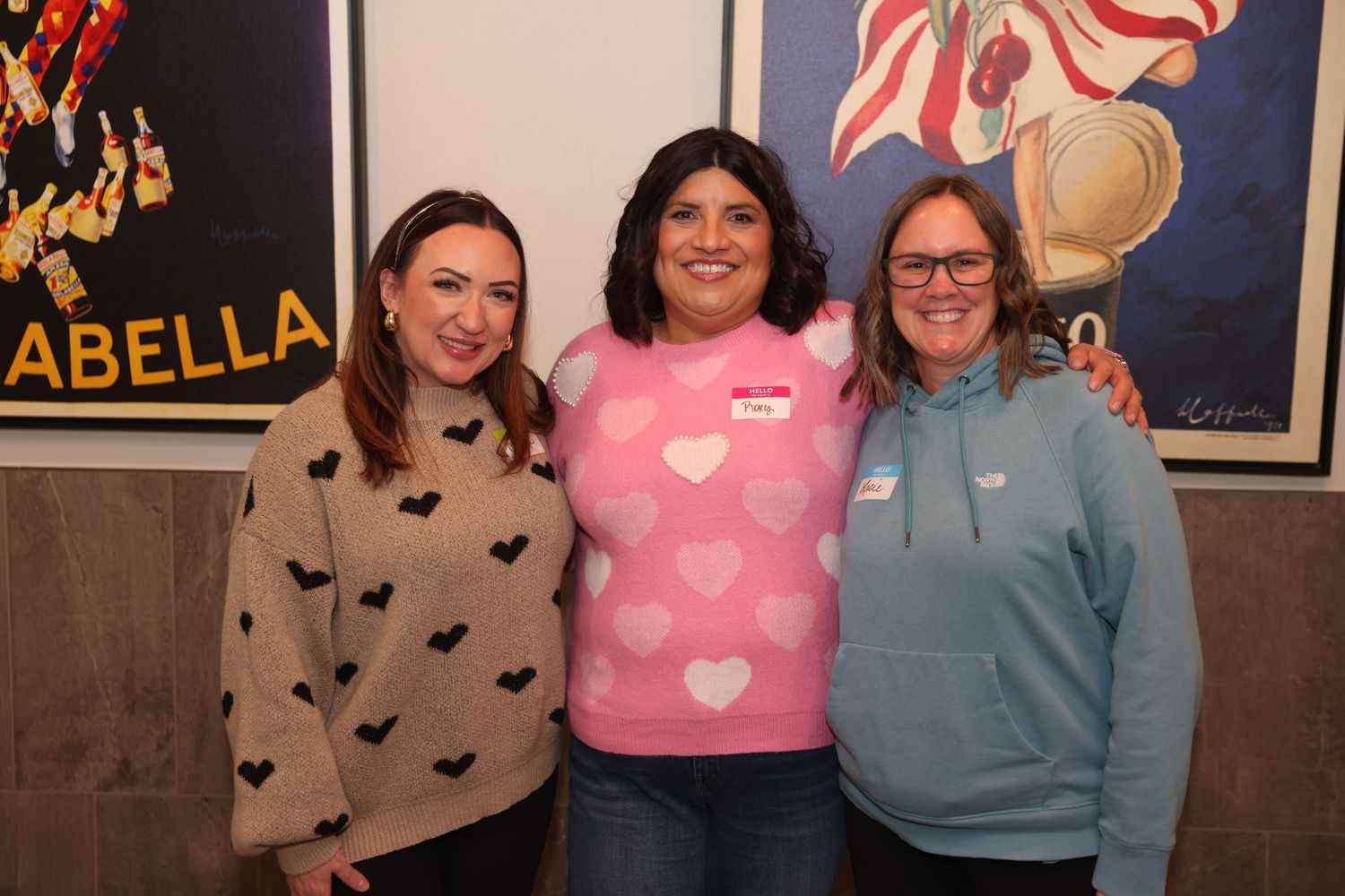 Group of people wearing cozy sweaters with heart and butterfly patterns gather together in a casual indoor setting.