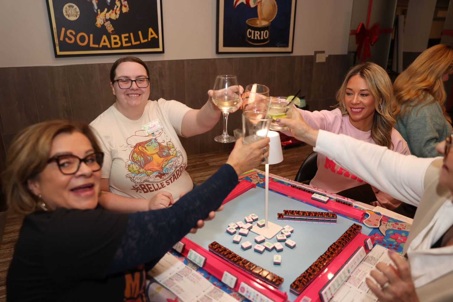 People gathered around a table playing mahjong with colorful tiles and racks during a social game night.