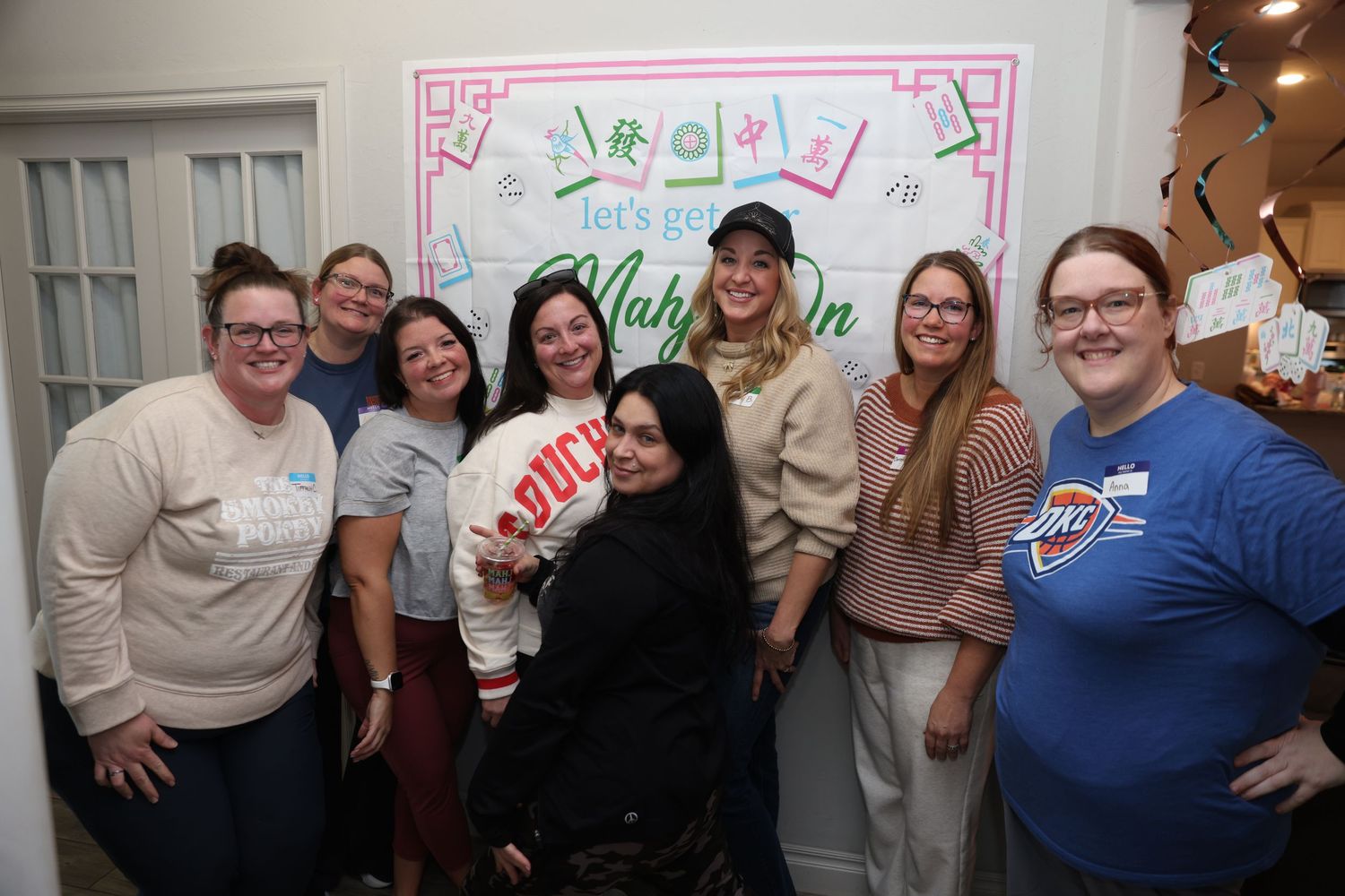 A group of people gathered together in a room with white walls and decorative artwork in the background.