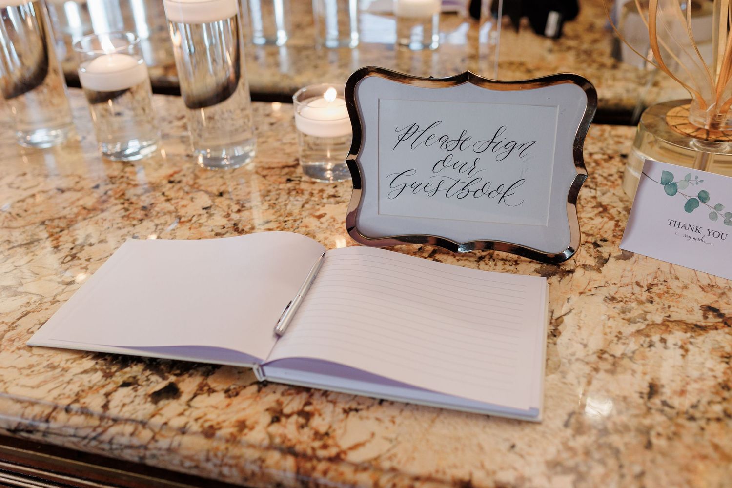 Wedding guest book open on granite table with elegant Please Sign Our Guestbook sign.