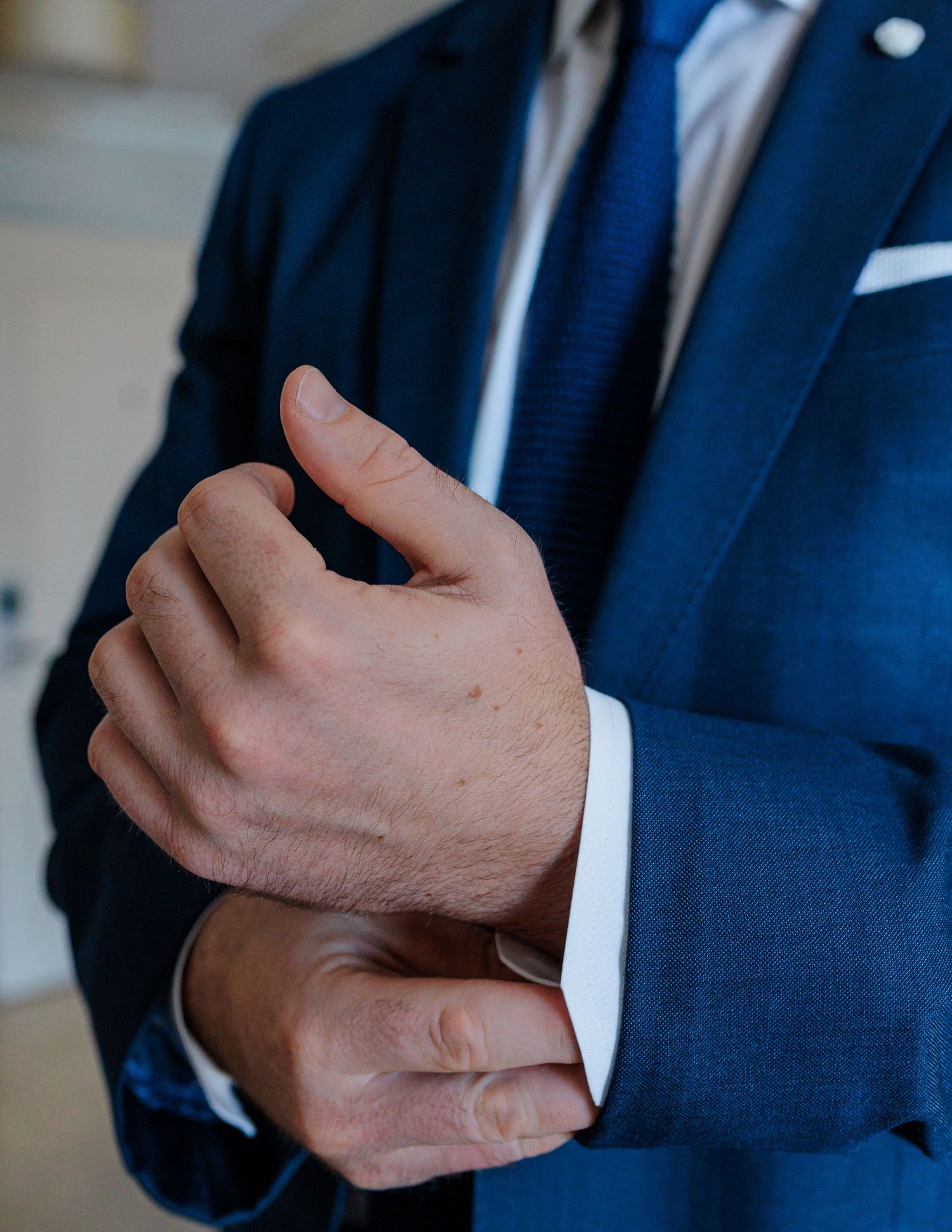Close-up of groom in navy blue suit adjusting cufflinks on white dress shirt before wedding.