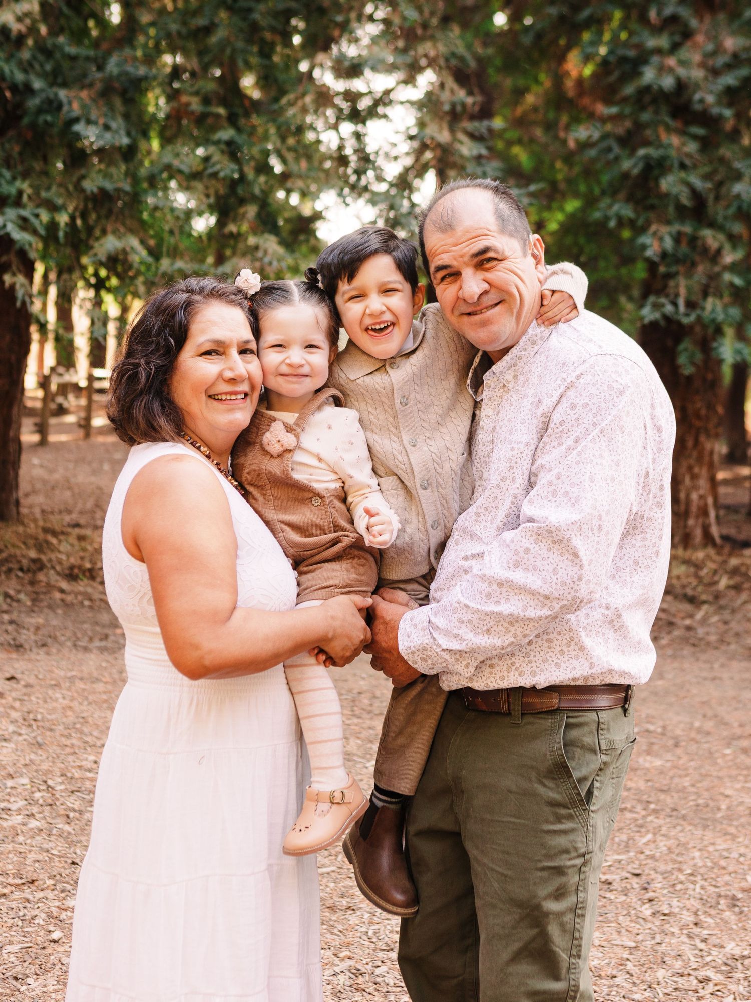 A happy family poses together outdoors on a dirt path surrounded by tall trees.