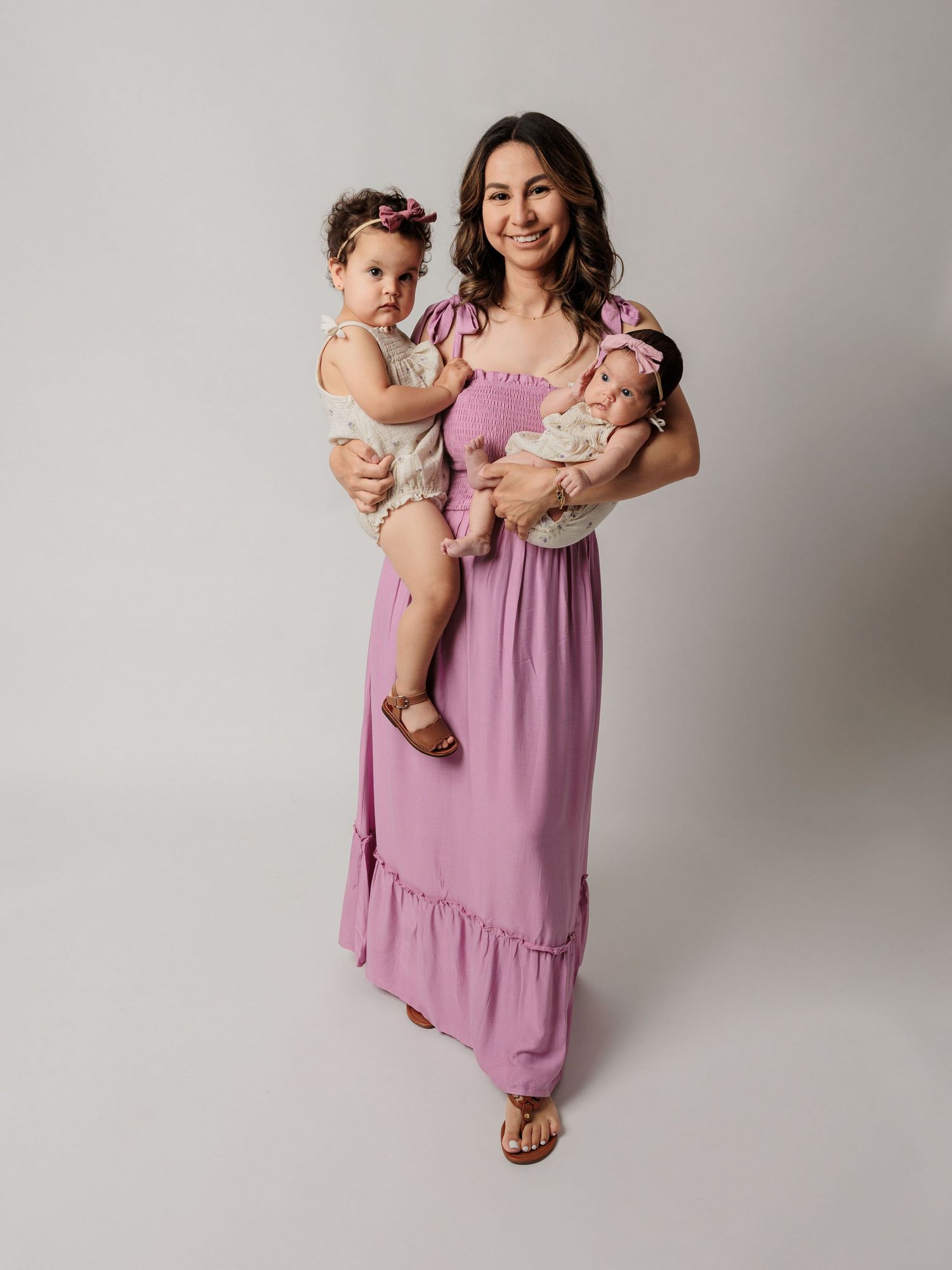 A parent holds two children while standing against a grey studio backdrop.